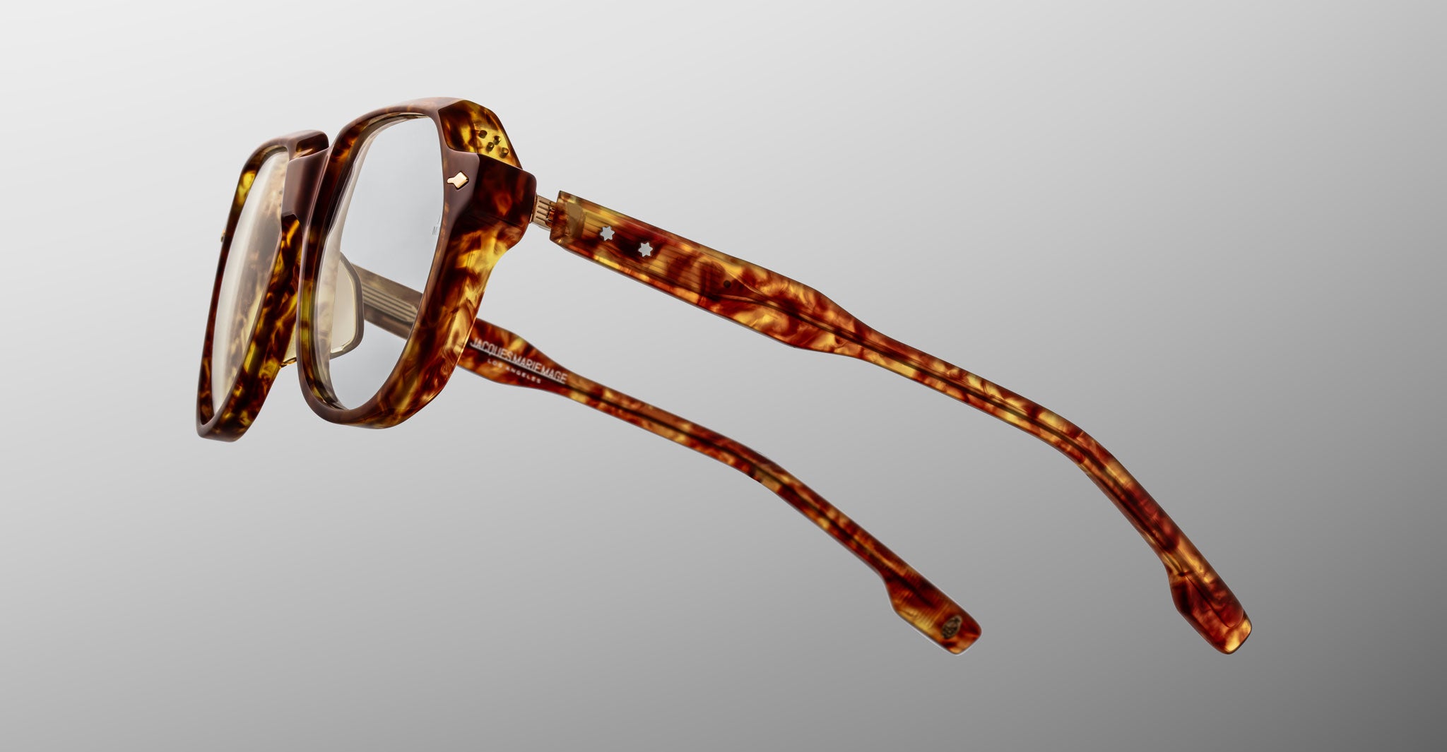 The Jacques Marie Mage Shozo eyeglasses feature thick, rectangular brown tortoiseshell frames with gently curved arms, shown against a light gray gradient background.