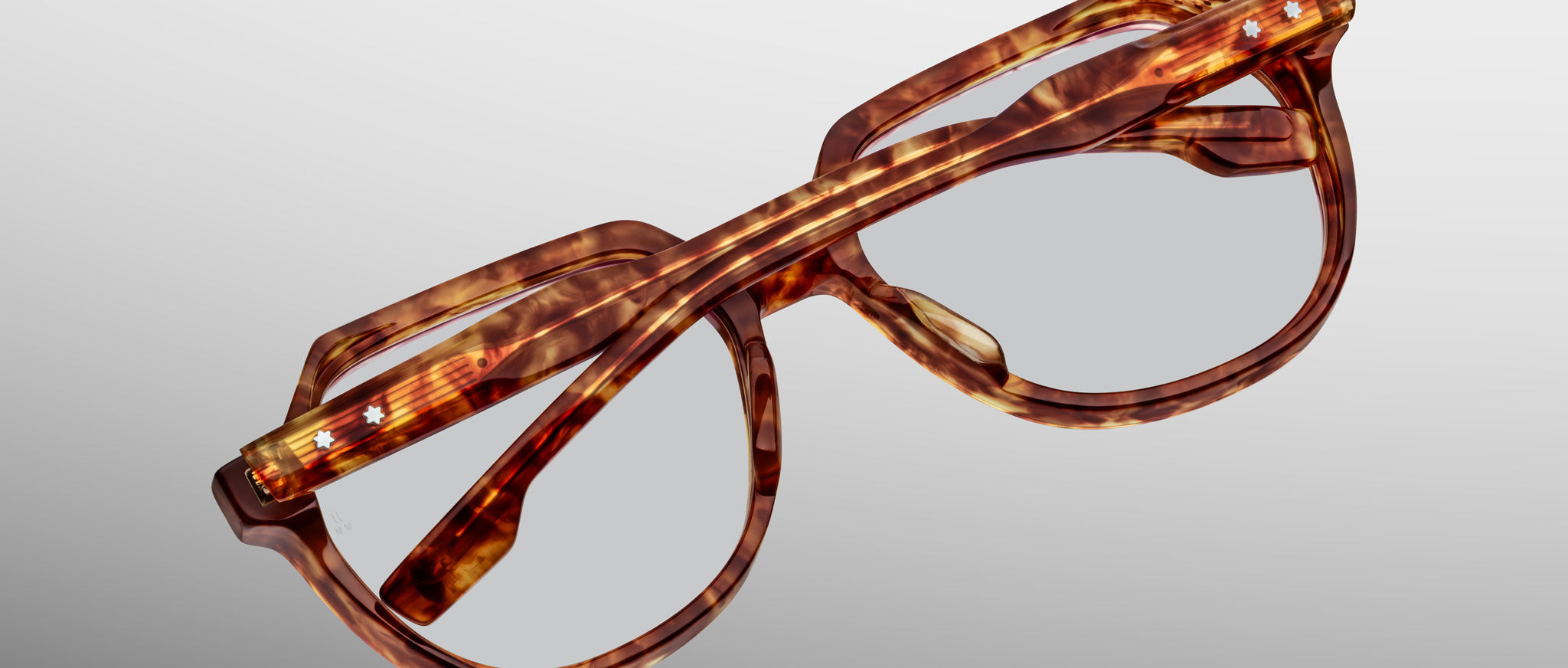 A pair of Jacques Marie Mage Shozo brown tortoiseshell eyeglasses with thick frames, folded upside down on a light gray background.