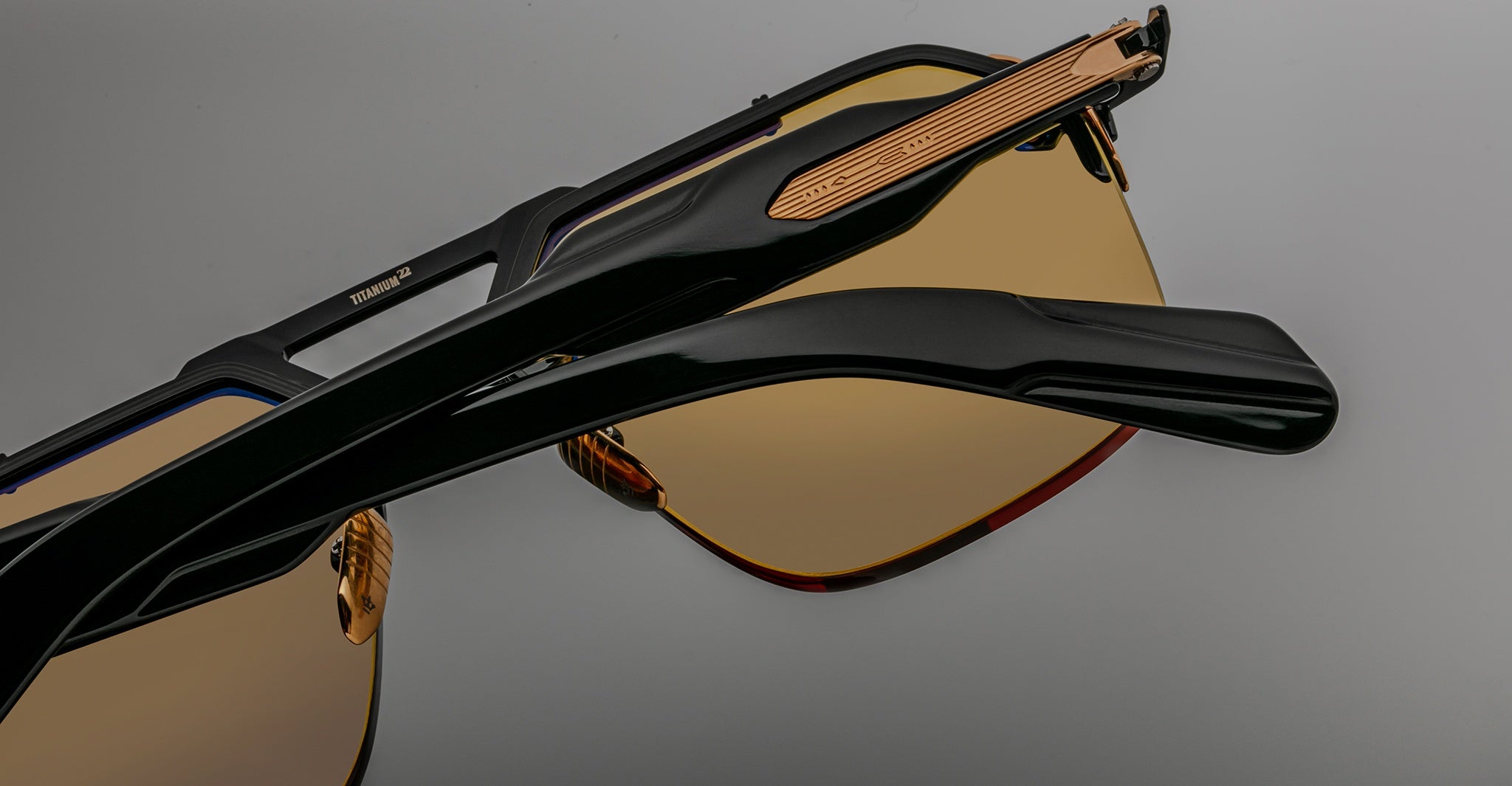 Close-up of two Jacques Marie Mage Silverton sunglasses with tinted lenses and black frames, stacked together on a gray background.