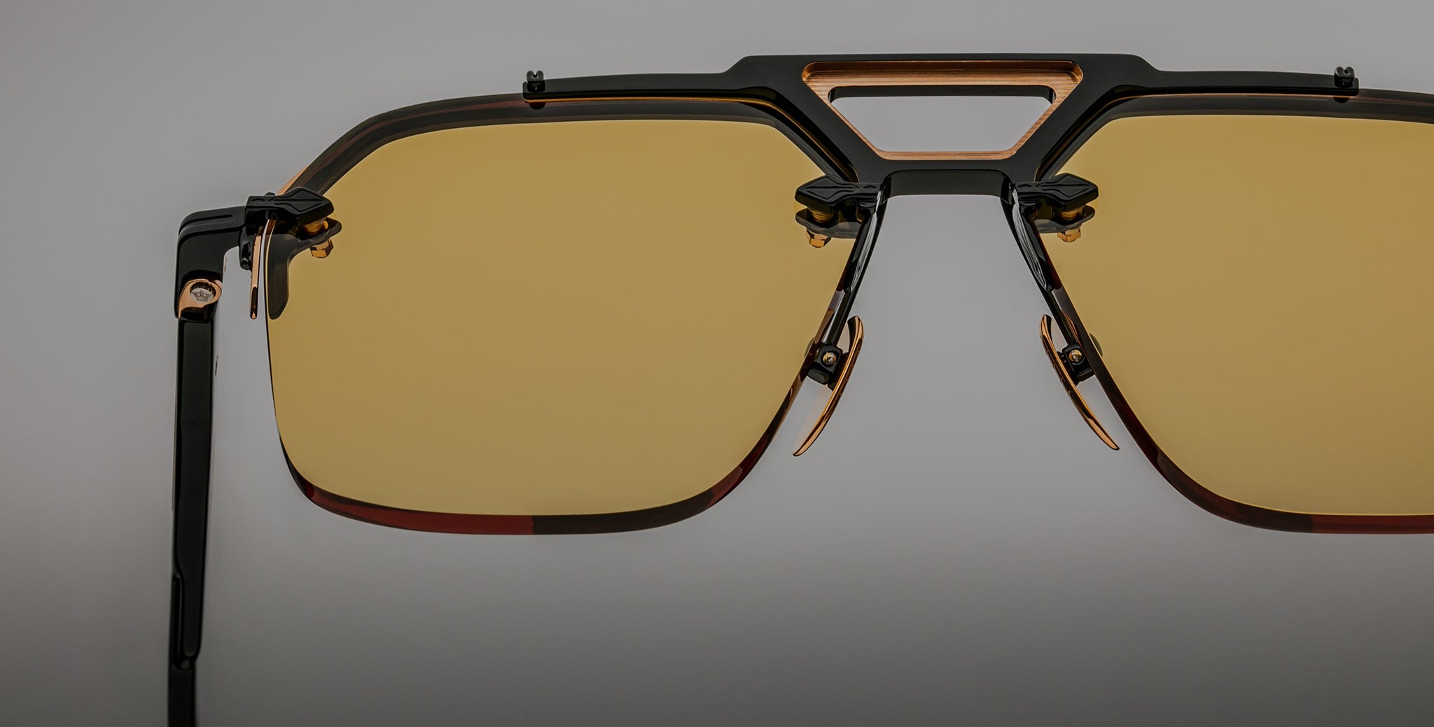 Close-up of Jacques Marie Mage Silverton sunglasses featuring yellow-tinted lenses, a geometric metal frame with black and gold accents, and adjustable nose pads on a neutral gray background.