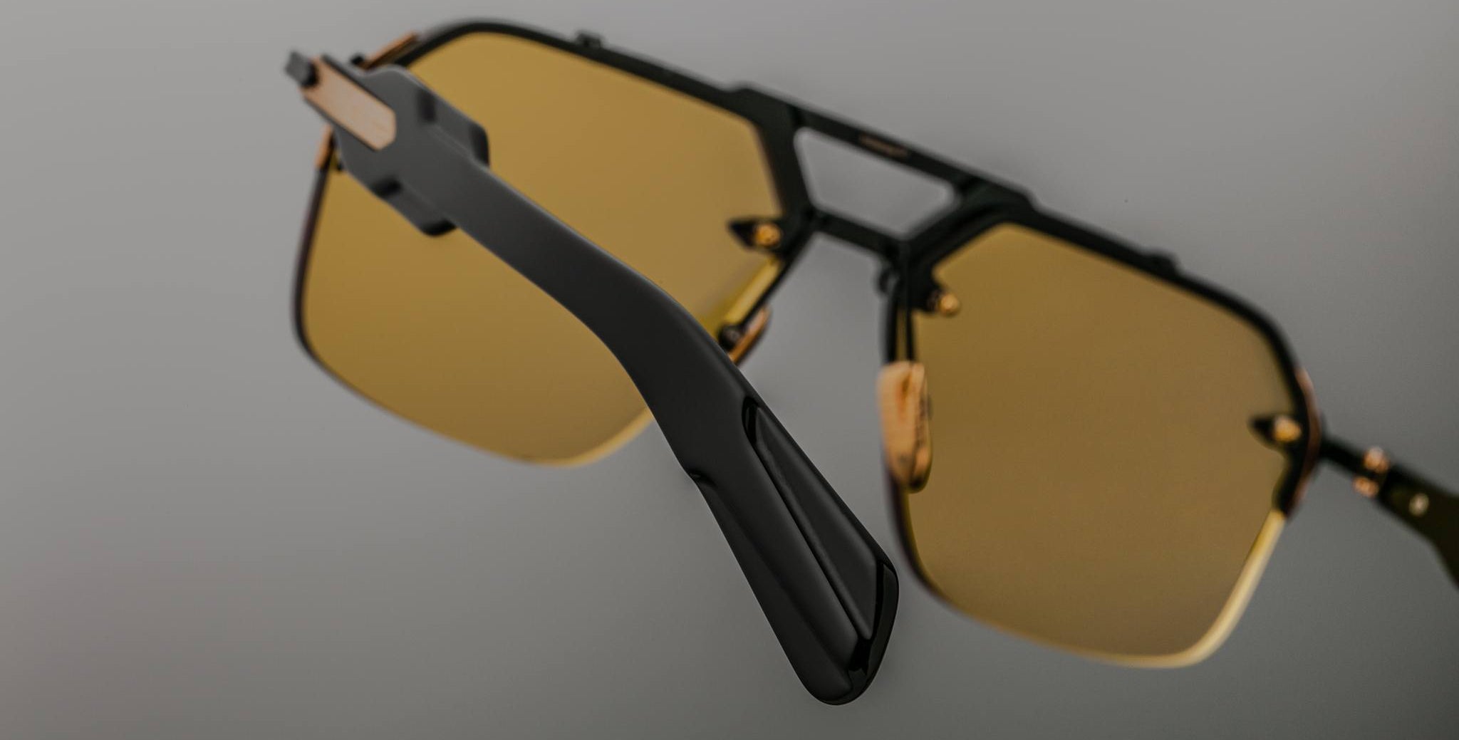 A close-up of the Jacques Marie Mage Silverton sunglasses featuring yellow-tinted lenses and black arms, set against a neutral gray background with focus on the side and front frames.