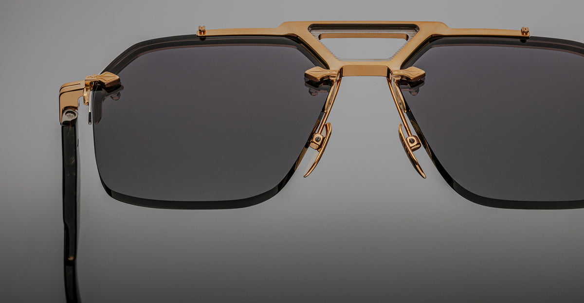 Close-up of Jacques Marie Mage Silverton sunglasses, featuring dark lenses and an intricate gold metal geometric frame with decorative accents above the nose bridge.