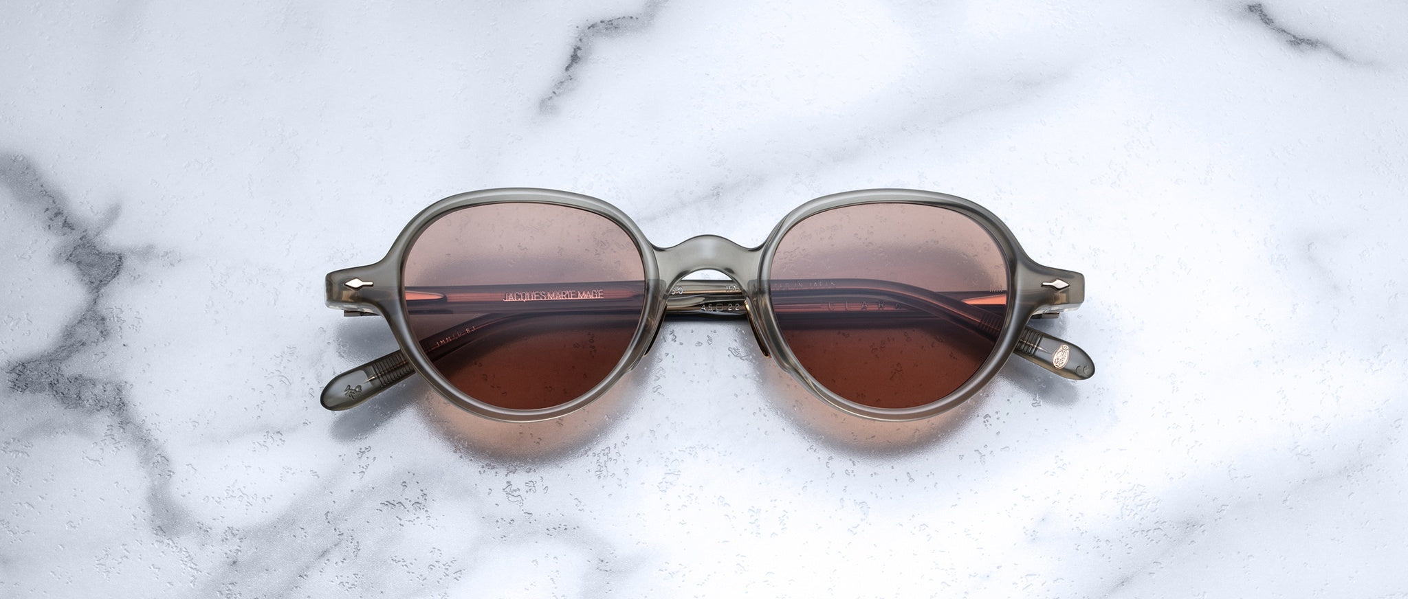 Jacques Marie Mage The Clark round sunglasses with brown UV lenses and clear frames, viewed from above.