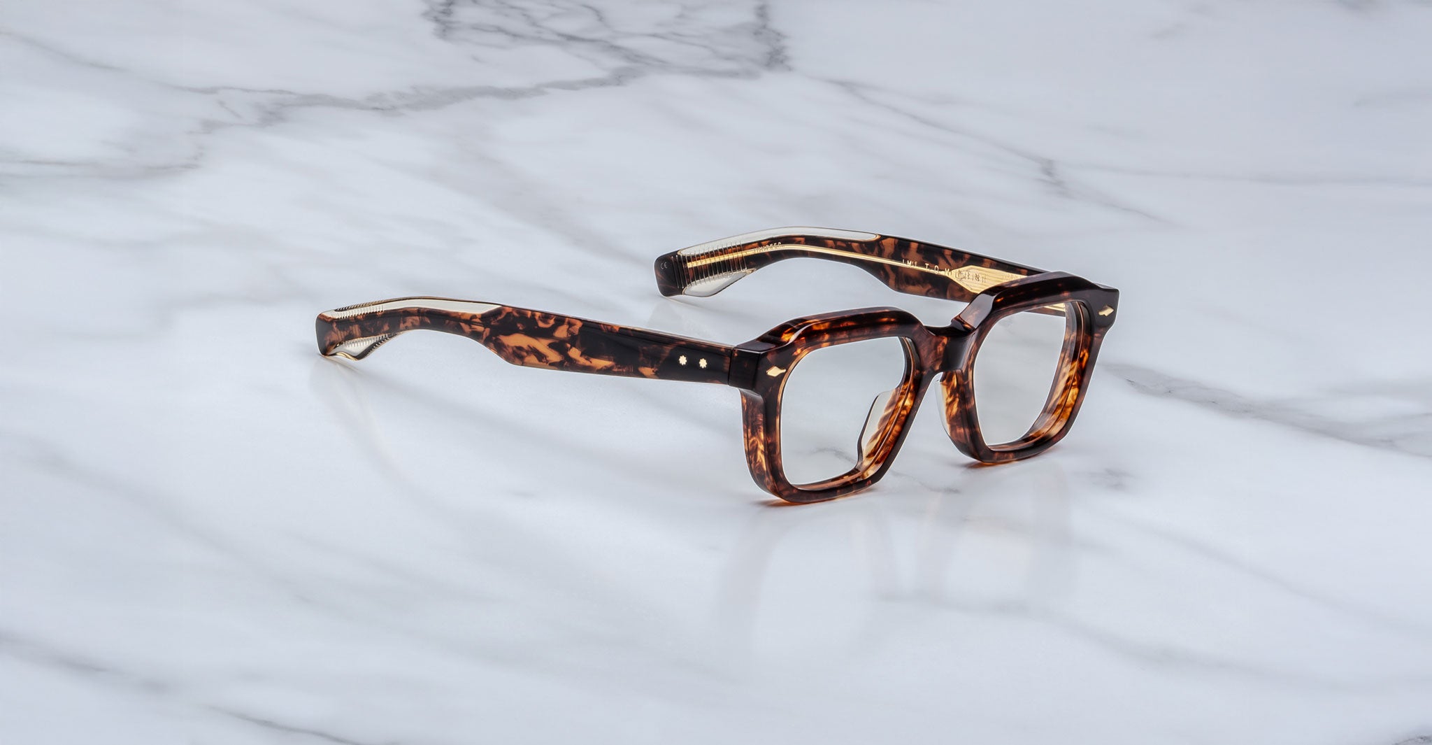 A pair of Jacques Marie Mage Tomlin brown tortoiseshell eyeglasses with thick rectangular frames and wide arms, displayed on a white marble surface.