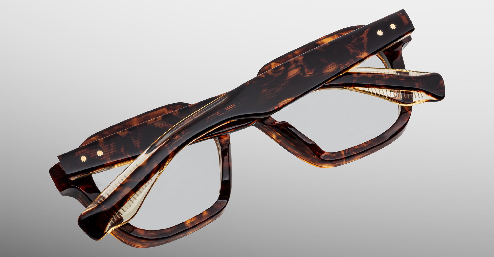 Two Jacques Marie Mage Tomlin eyeglasses with tortoiseshell-patterned rectangular frames are stacked atop each other against a plain light gray background.