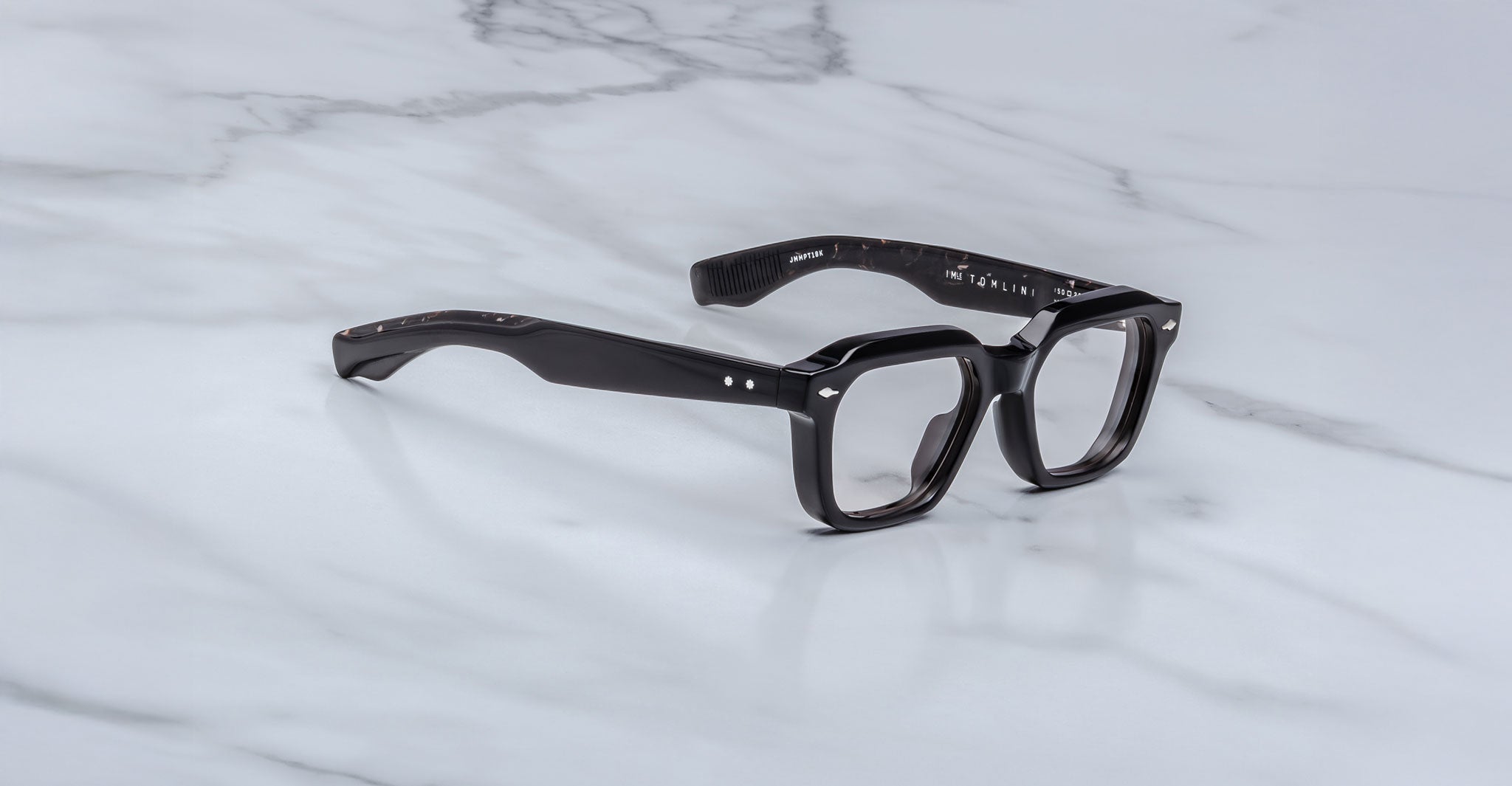Jacques Marie Mage Tomlin rectangular black eyeglasses with thick frames and silver side accents, displayed on a white marble surface.