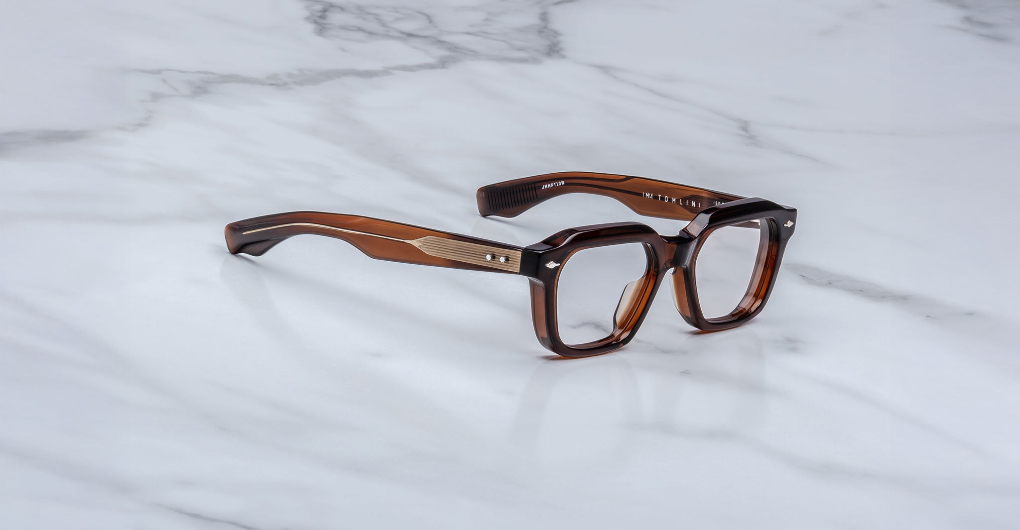 A pair of Jacques Marie Mage Tomlin eyeglasses featuring thick brown rectangular frames and sturdy arms, displayed on a white marble surface.