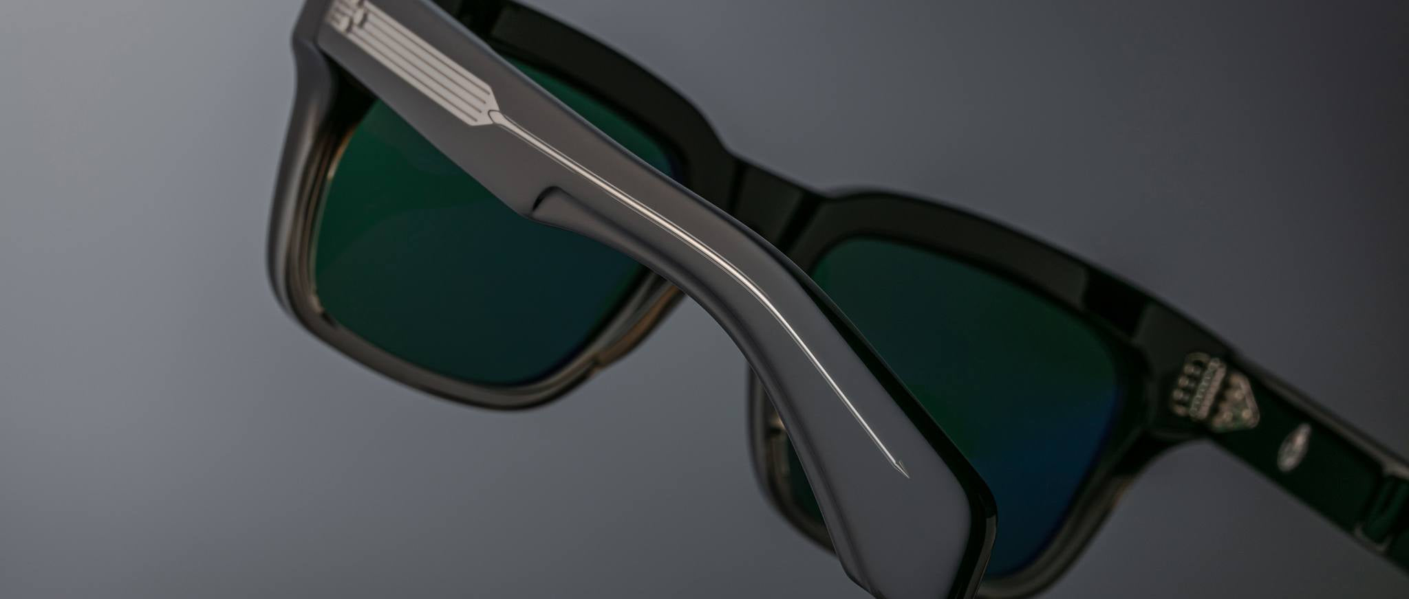 Close-up of Jacques Marie Mage Torino rectangular eyeglass frames in black, featuring green-tinted lenses, handcrafted acetate construction, detailed side arms, and a small logo on the lens.