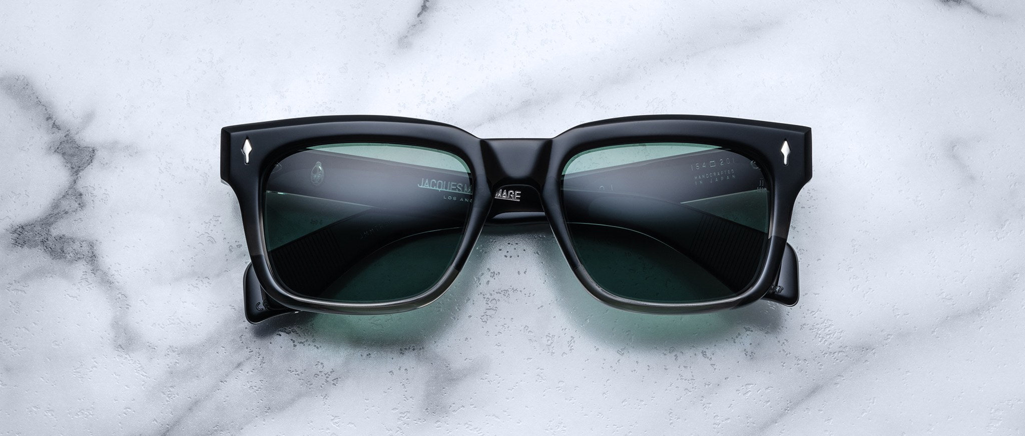 Jacques Marie Mage Torino: Bold, handcrafted black rectangular sunglasses with dark lenses by Jacques Marie Mage, styled on a white marble surface.
