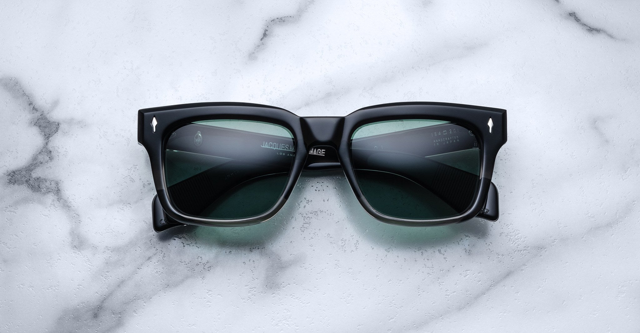 Jacques Marie Mage Torino: Bold, handcrafted black rectangular sunglasses with dark lenses by Jacques Marie Mage, styled on a white marble surface.