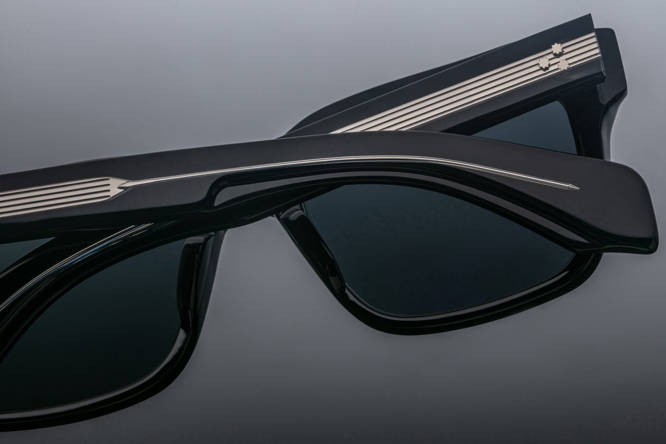 Close-up of two pairs of Jacques Marie Mage Torino handcrafted acetate eyeglasses with silver striped arm detailing, overlapping on a gray surface. These bold rectangular frames showcase the signature Jacques Marie Mage style.