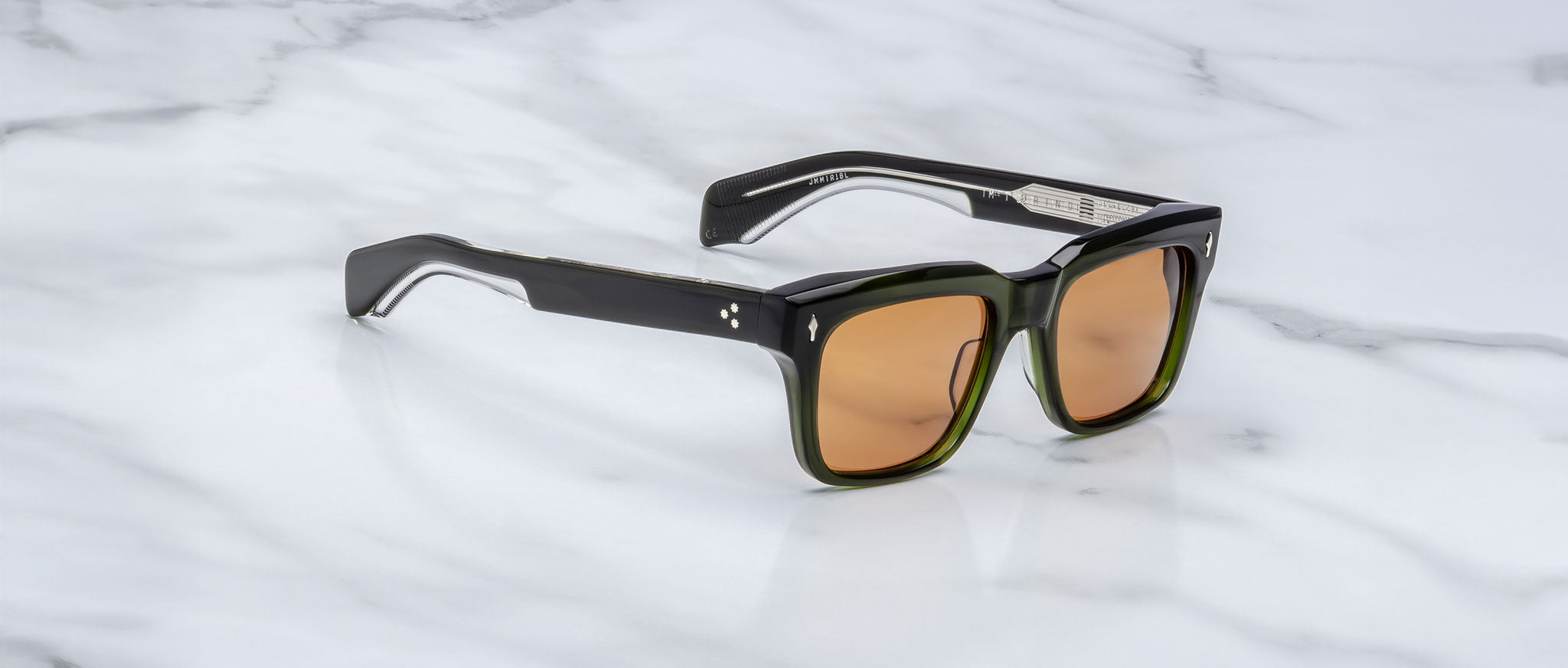 The Jacques Marie Mage Torino sunglasses feature bold, dark green rectangular acetate frames and amber-tinted lenses, inspired by the brand's signature style and displayed on a white marble surface.