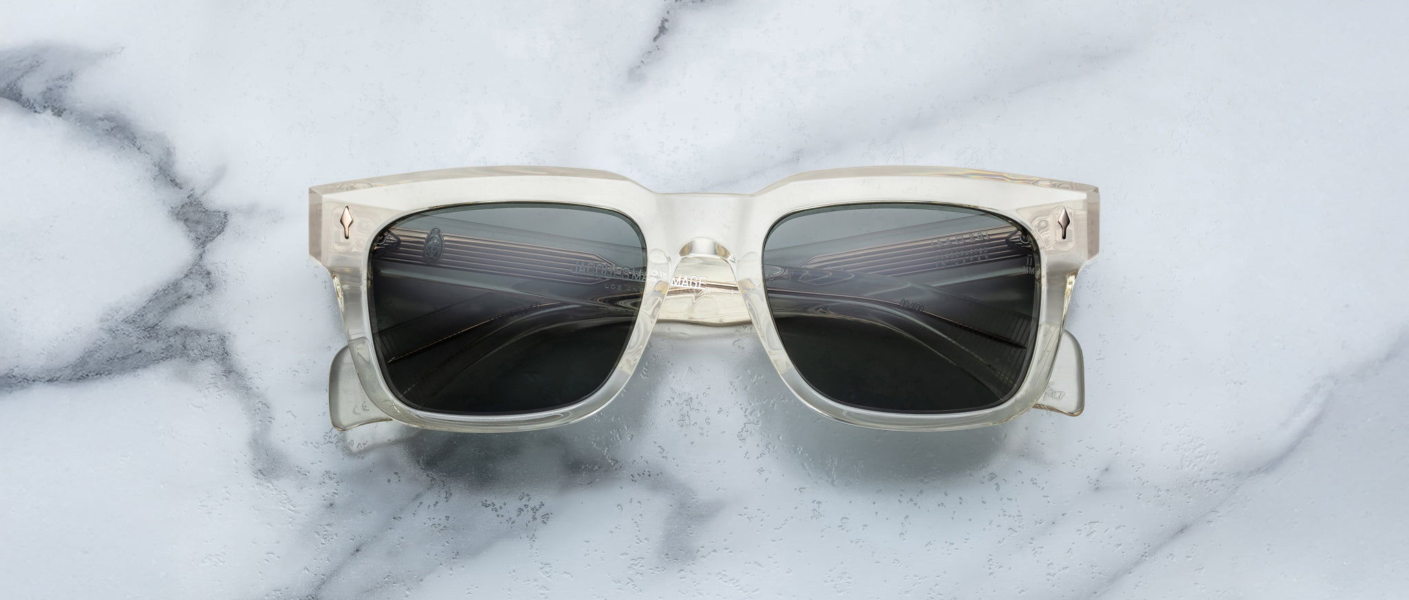 Jacques Marie Mage Torino eyeglasses by Jacques Marie Mage feature bold clear rectangular frames with dark lenses, displayed on a white marble surface.