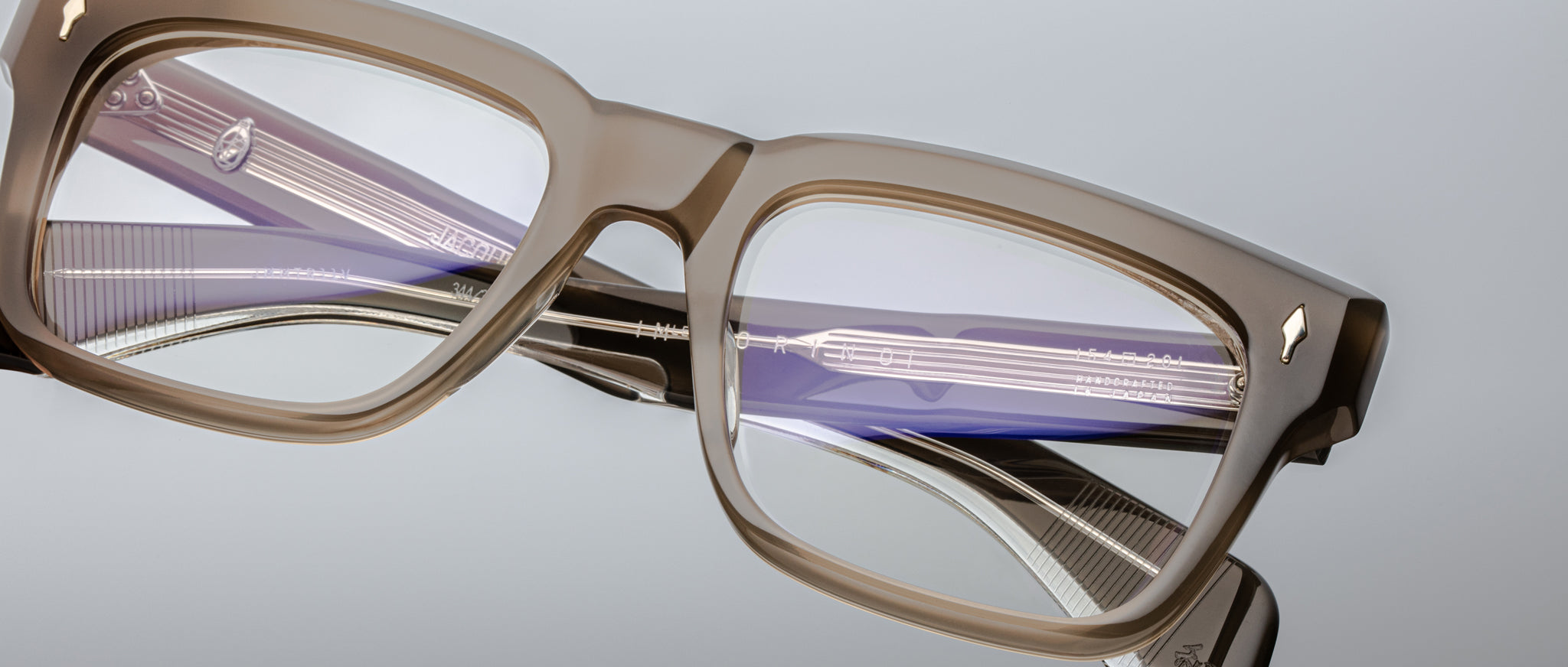 Close-up of Jacques Marie Mage Torino eyeglasses, bold rectangular frames in handcrafted acetate with clear lenses, reflective details, and Jacques Marie Mage branding on the temples.