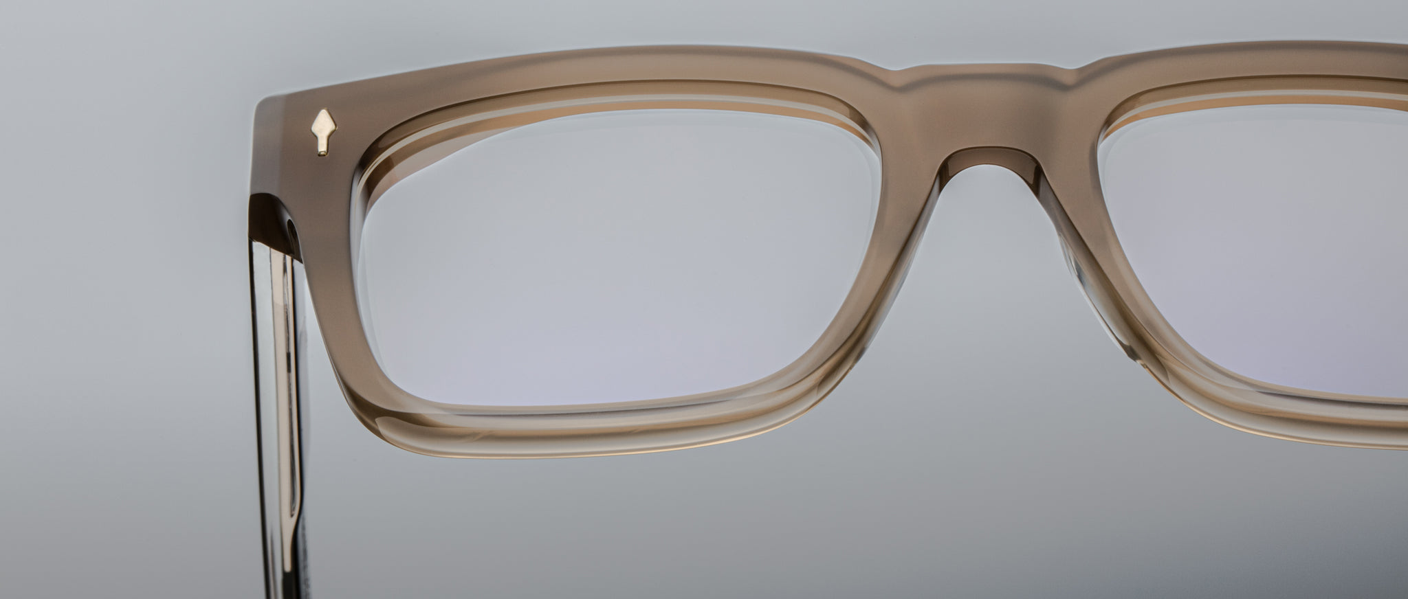 Close-up of the upper section of rectangular Jacques Marie Mage Torino eyeglass frames, featuring handcrafted translucent brown acetate, set against a plain light background.