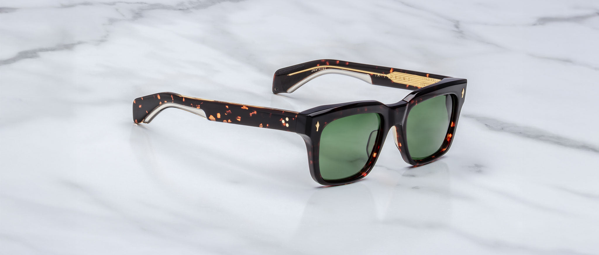Jacques Marie Mage Torino sunglasses by Jacques Marie Mage feature bold rectangular tortoiseshell frames and green lenses, reminiscent of handcrafted acetate eyewear, displayed on a white marble surface.