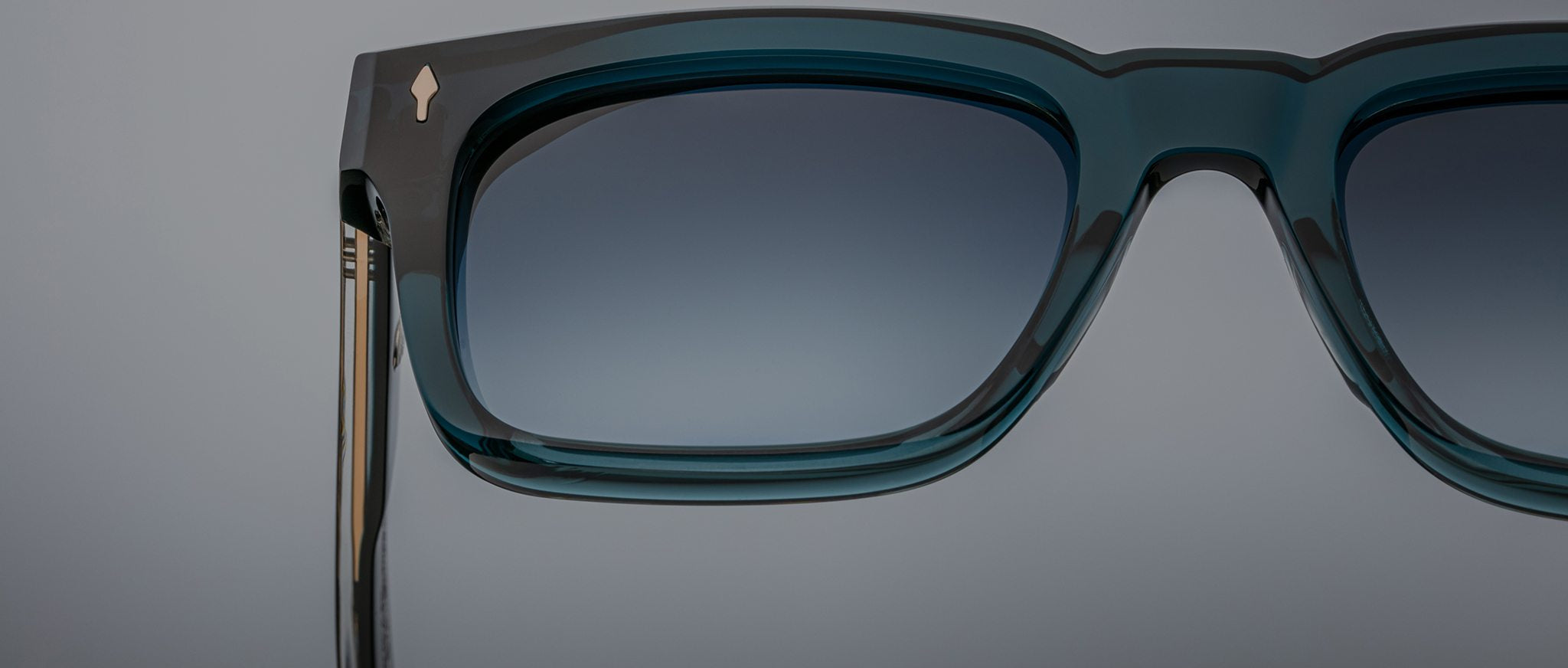 Close-up of Jacques Marie Mage Torino eyeglasses: bold, handcrafted acetate frames in teal with gradient-tinted lenses by Jacques Marie Mage, set against a plain gray background.