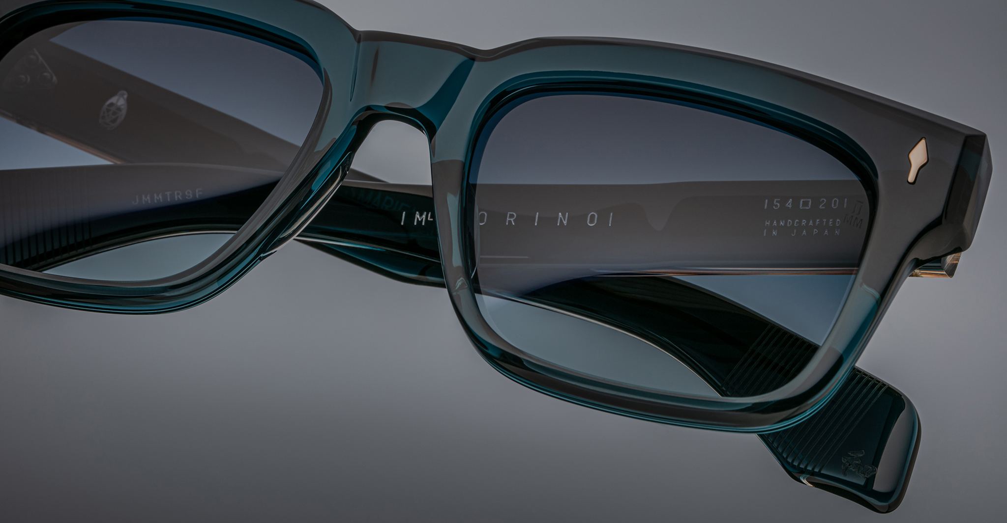 Close-up of Jacques Marie Mage Torino rectangular eyeglass frames, handcrafted acetate eyewear featuring brand markings on the inner arm, shown against a gray background.
