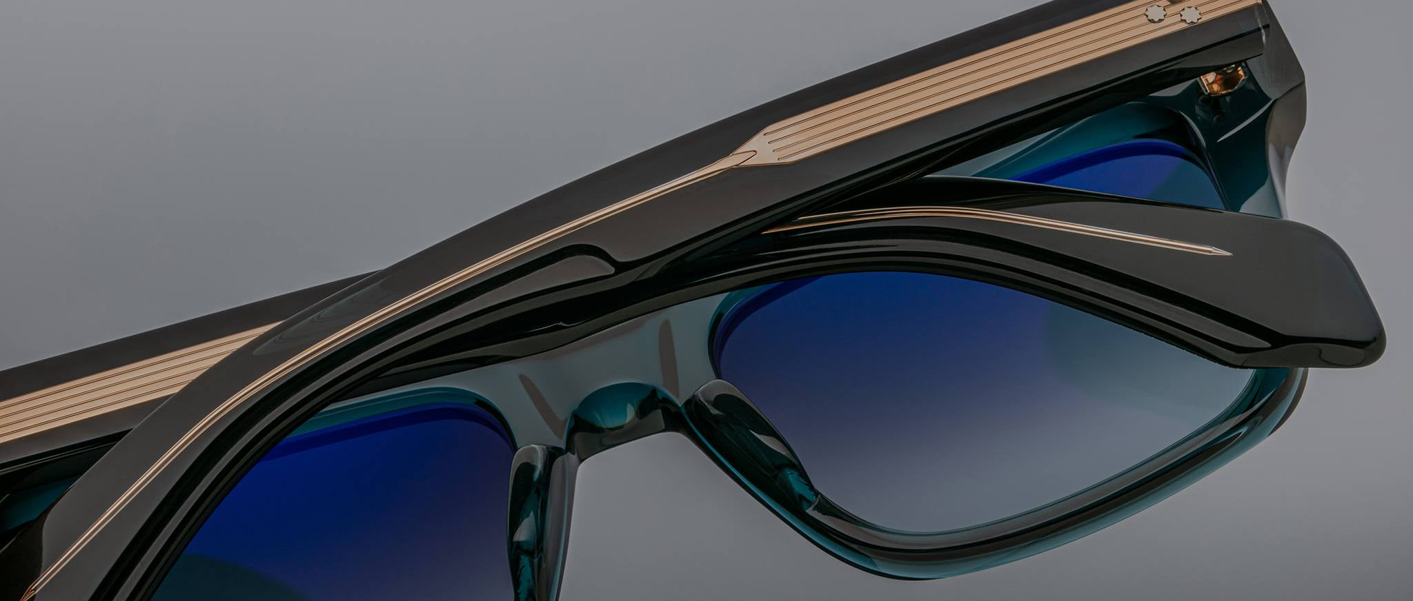 Close-up of two pairs of Jacques Marie Mage Torino sunglasses by Jacques Marie Mage, featuring bold rectangular frames with gold detailing on the arms, stacked diagonally against a gray background.