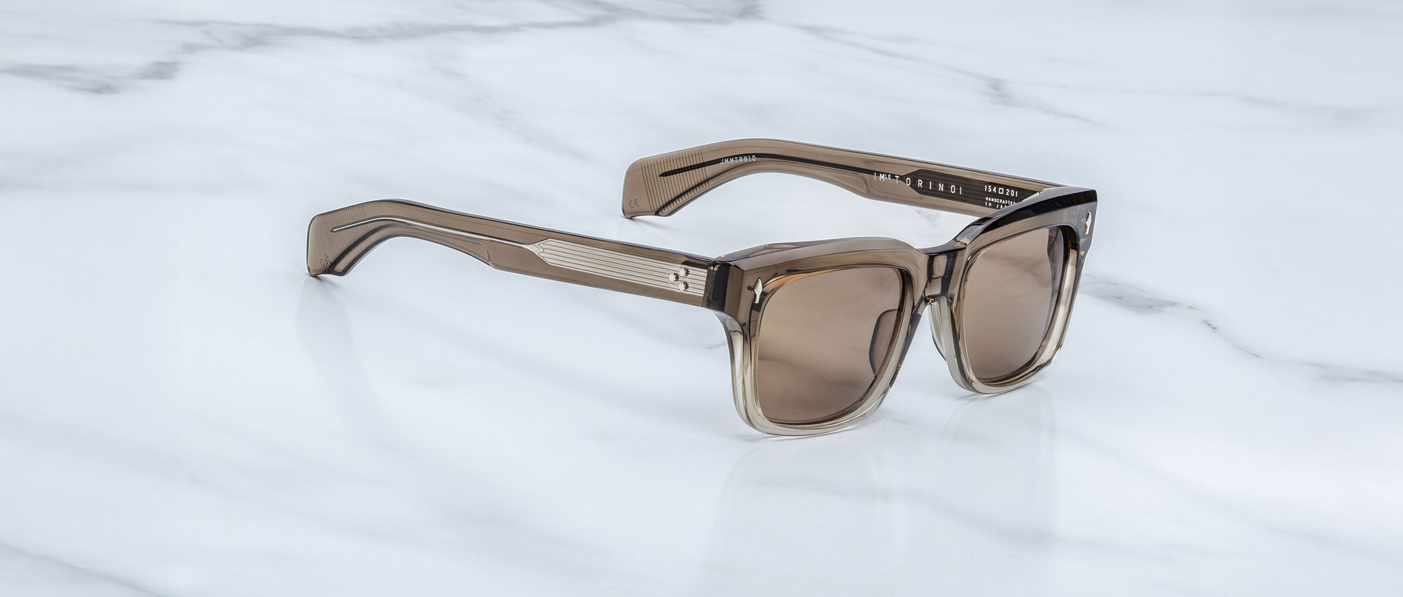 A pair of Jacques Marie Mage Torino sunglasses by Jacques Marie Mage, with bold rectangular brown translucent frames, rests on a white marble surface.