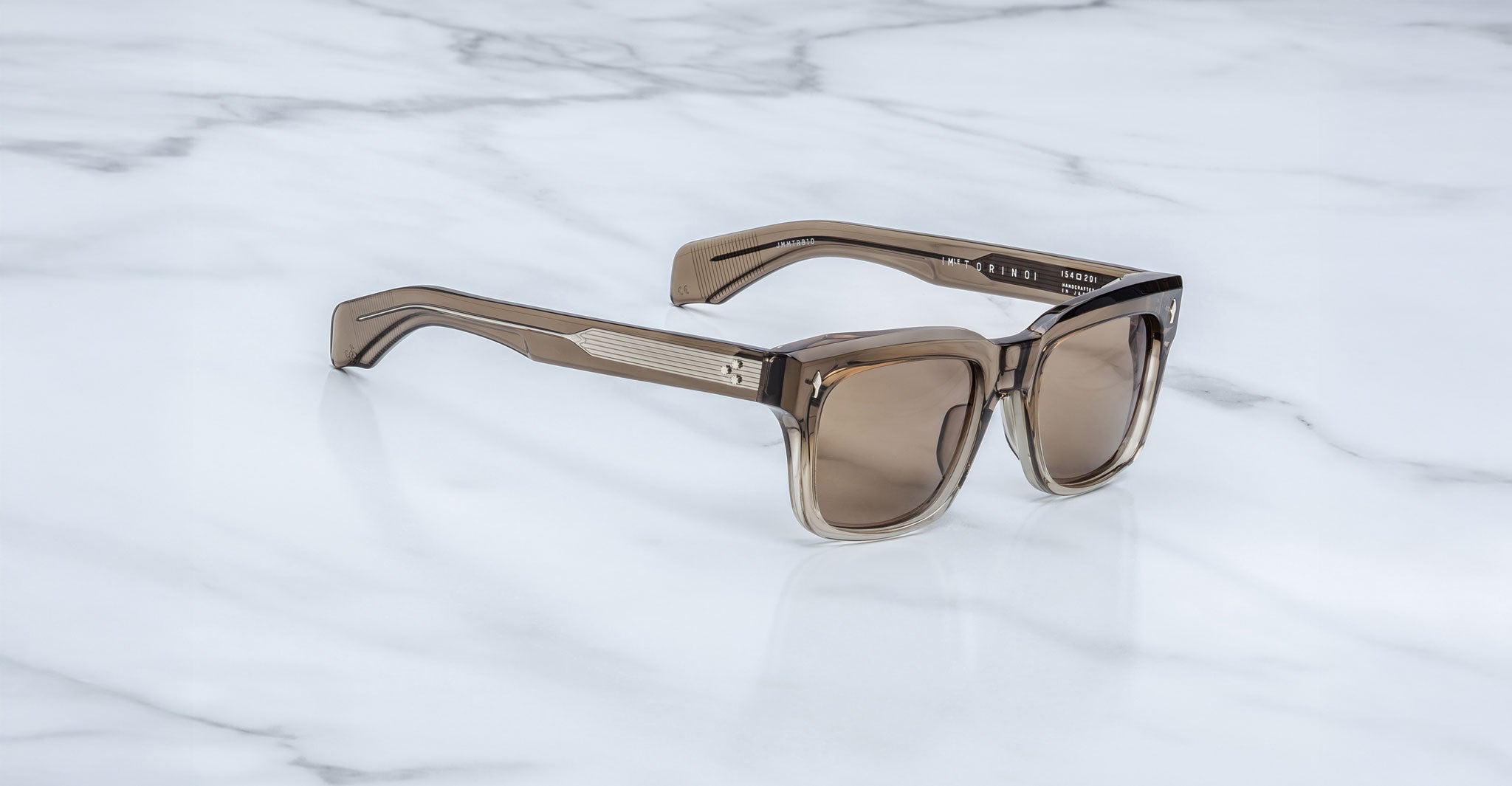 A pair of Jacques Marie Mage Torino sunglasses by Jacques Marie Mage, with bold rectangular brown translucent frames, rests on a white marble surface.