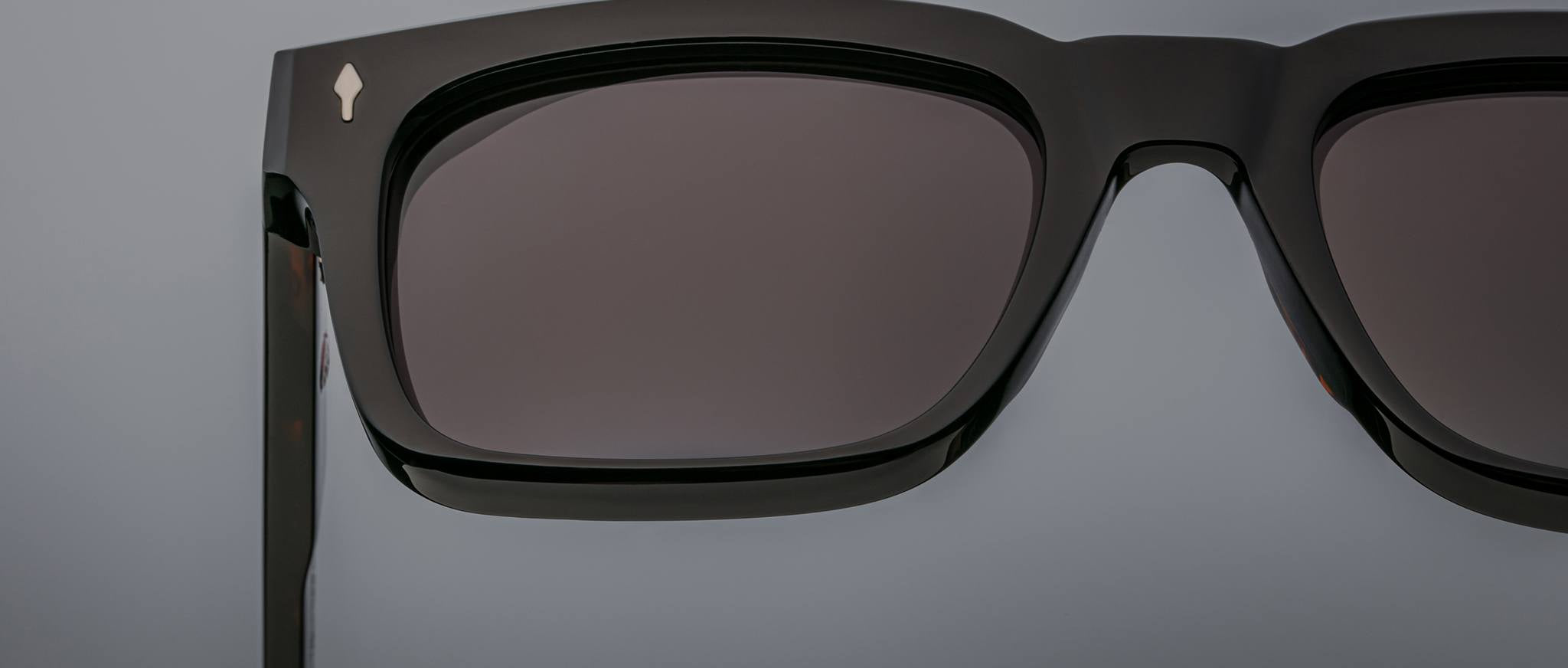 Close-up of Jacques Marie Mage Torino sunglasses featuring bold rectangular black acetate frames, dark lenses, and hinges, set against a neutral background.