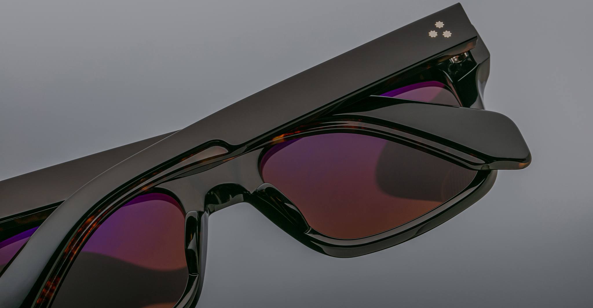 Close-up of Jacques Marie Mage Torino rectangular eyeglass frames, featuring dark tinted lenses and a subtle decorative accent on handcrafted acetate, inspired by the iconic style of Jacques Marie Mage, set against a gray background.