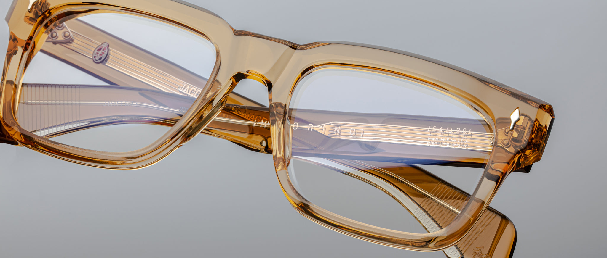 The Jacques Marie Mage Torino, bold rectangular eyeglass frames in amber transparent acetate by Jacques Marie Mage, rest on a light gray surface—a striking example of handcrafted acetate eyewear.