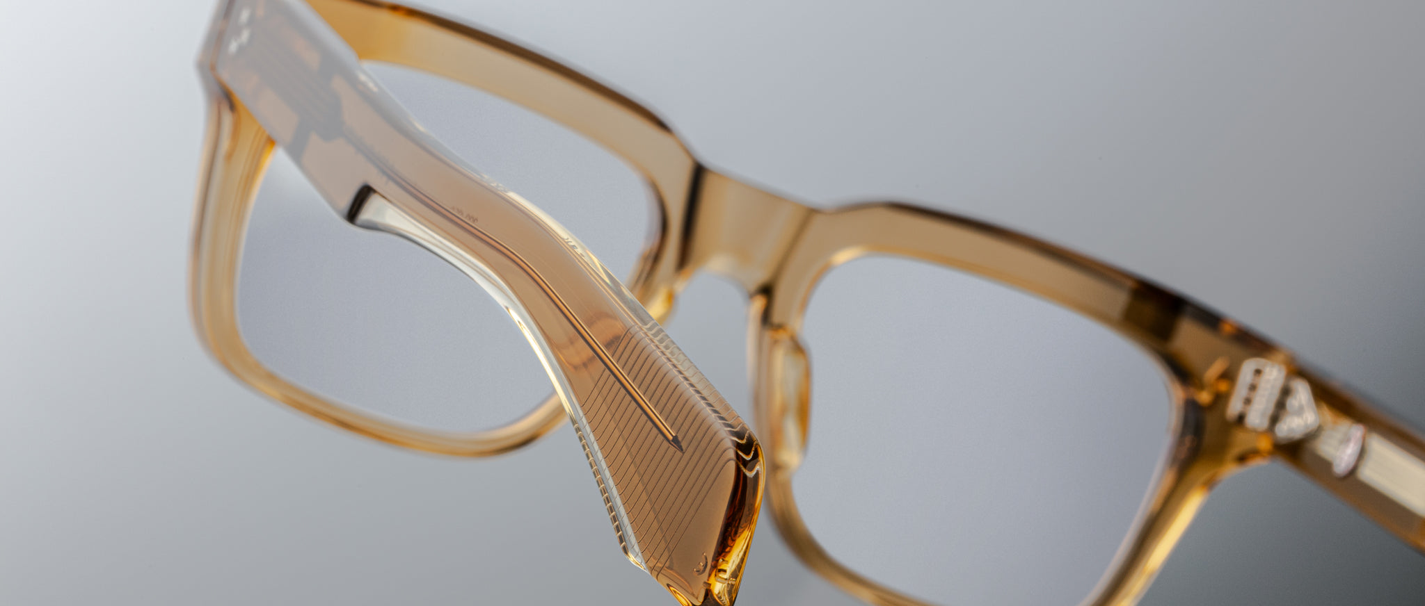 Close-up of Jacques Marie Mage Torino eyeglasses, featuring bold, rectangular frames in light brown translucent handcrafted acetate with clear lenses, shown against a neutral background.