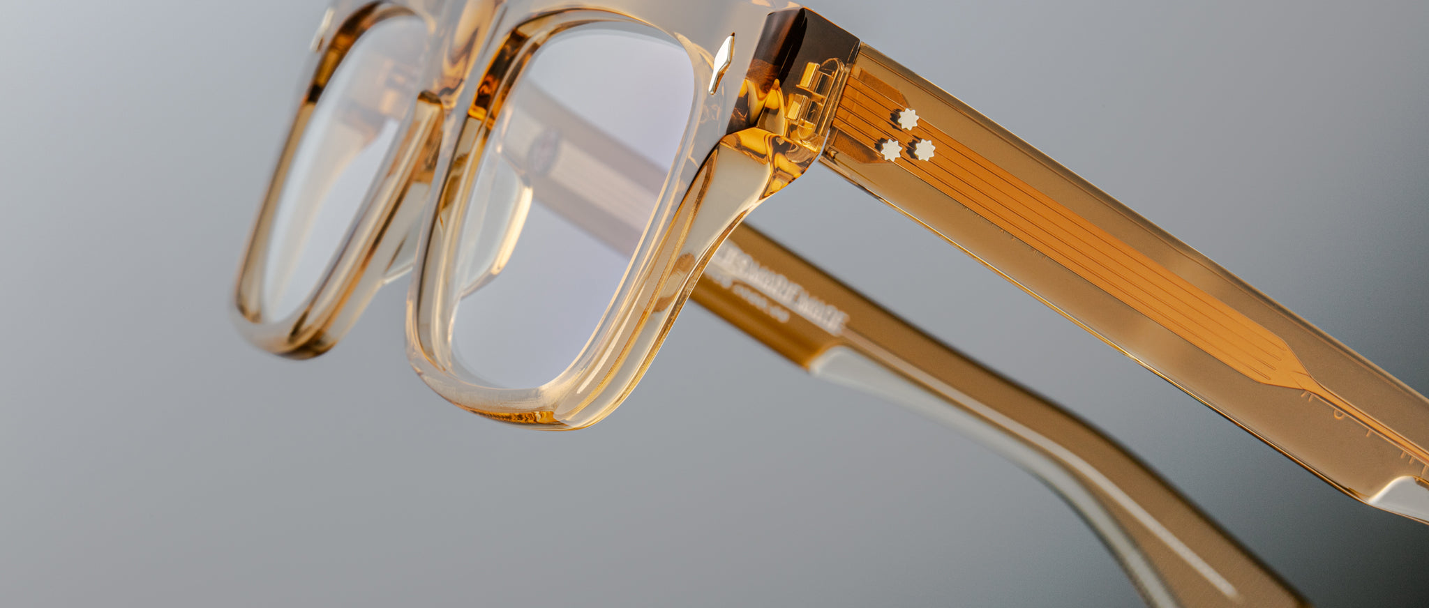 The Jacques Marie Mage Torino by Jacques Marie Mage is a thick, clear-framed rectangular eyeglass in translucent amber acetate, inspired by bold designs and shown close up against a neutral background.