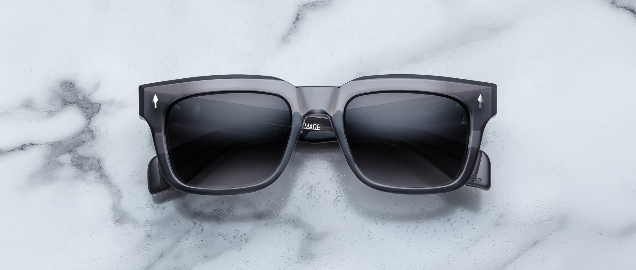 Jacques Marie Mage Torino sunglasses by Jacques Marie Mage, featuring bold rectangular black frames and dark lenses, displayed on a white marble surface.
