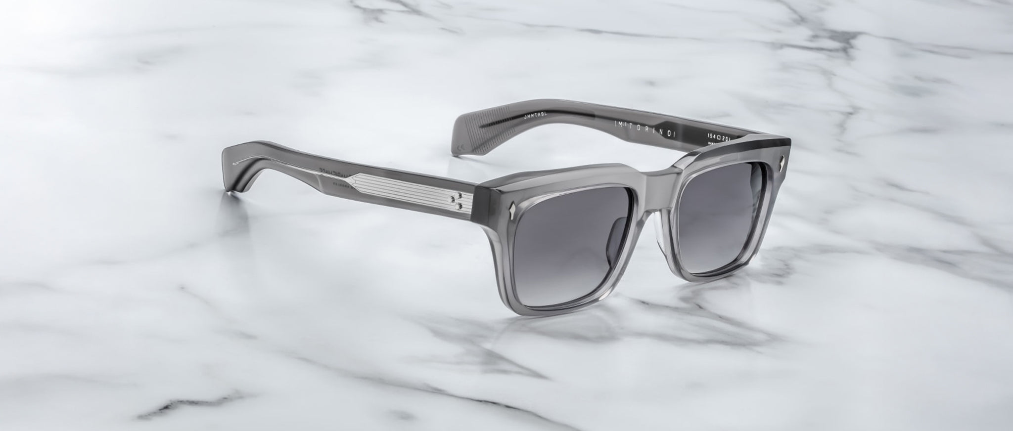 Jacques Marie Mage Torino rectangular sunglasses with dark lenses and bold handcrafted acetate frames rest on a white marble surface.