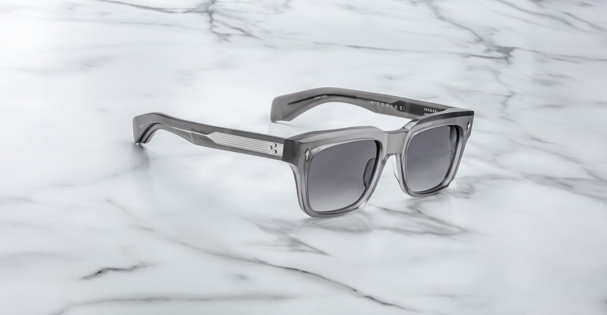 Jacques Marie Mage Torino rectangular sunglasses with dark lenses and bold handcrafted acetate frames rest on a white marble surface.