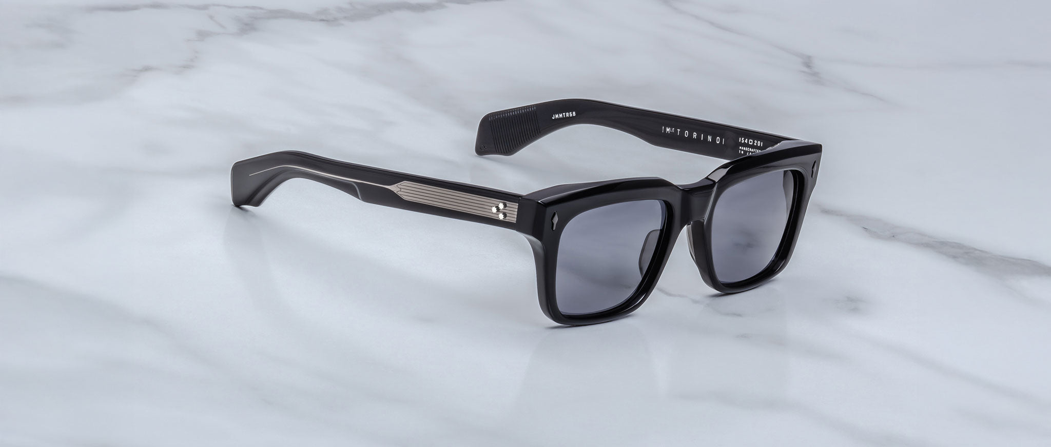Showcasing the artistry of handcrafted acetate, Jacques Marie Mage Torino features bold black rectangular frames with dark lenses and metal temple accents, displayed on a white marble surface.