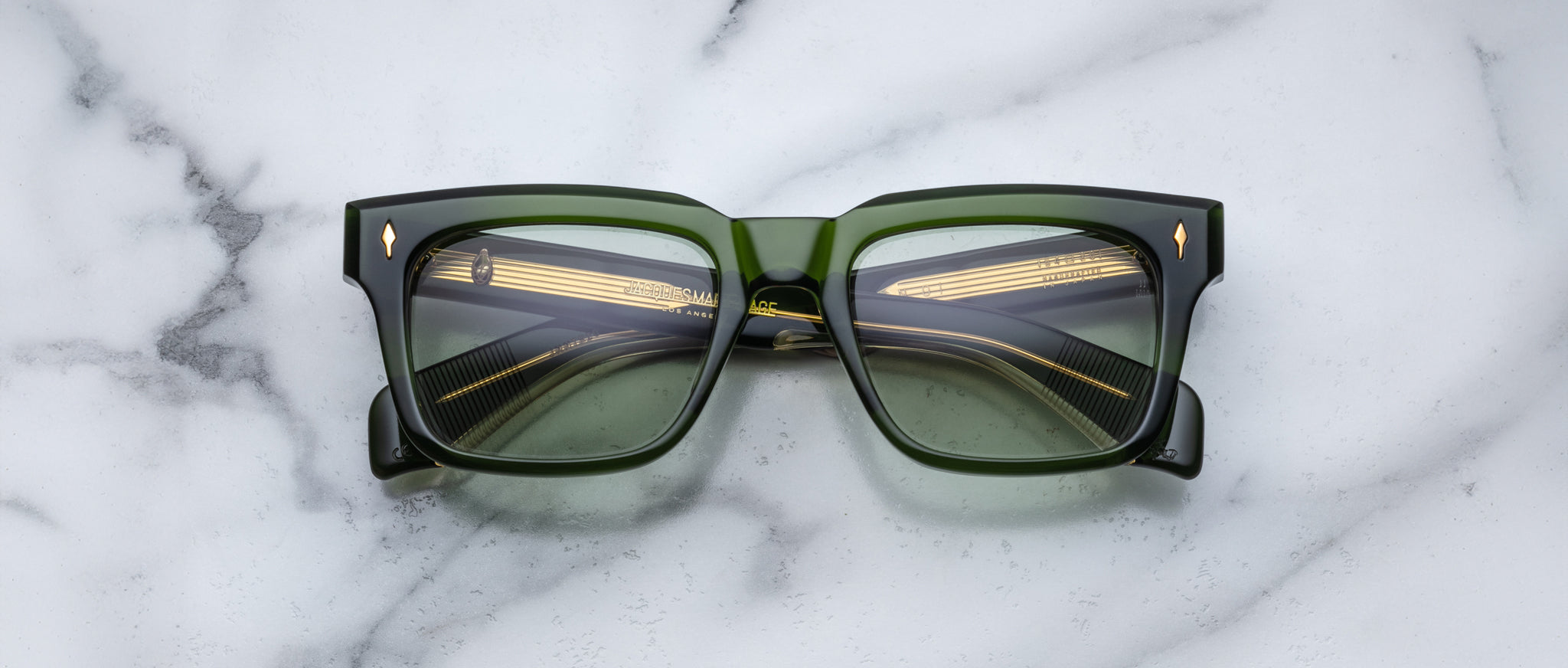 A pair of Jacques Marie Mage Torino rectangular eyeglass frames in bold green handcrafted acetate with dark lenses, inspired by the brand's signature style, displayed on a white marble surface.