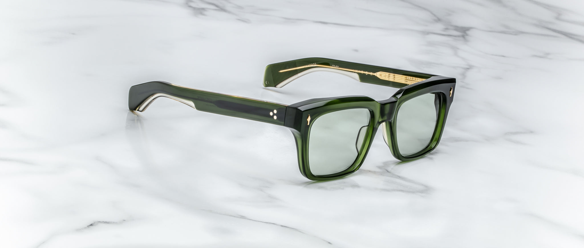 Jacques Marie Mage Torino sunglasses by Jacques Marie Mage, featuring a bold green rectangular design with gold accents, are displayed on a white marble surface.
