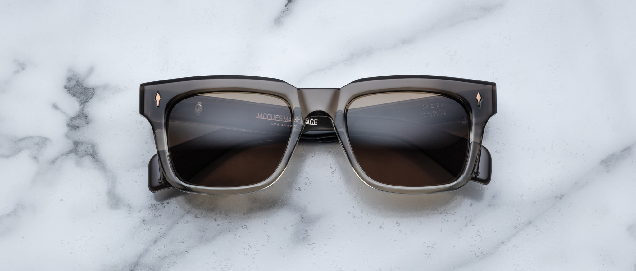 The Jacques Marie Mage Torino, bold rectangular eyeglass frames in dark brown handcrafted acetate by Jacques Marie Mage, rests on a white marble surface.