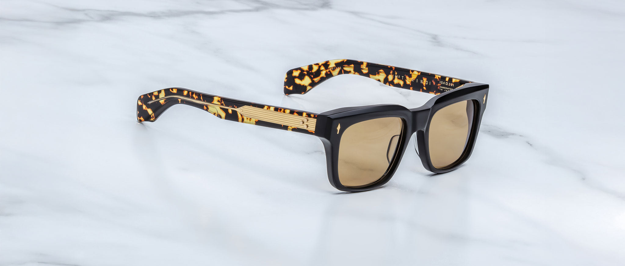 The Jacques Marie Mage Torino sunglasses feature bold rectangular acetate frames, brown tinted lenses, and tortoiseshell-patterned arms, handcrafted by Jacques Marie Mage and displayed on a white marble surface.