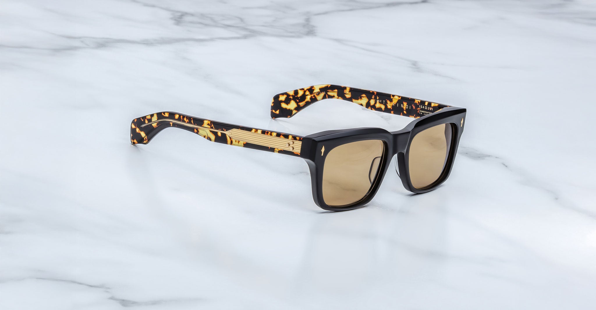 The Jacques Marie Mage Torino sunglasses feature bold rectangular acetate frames, brown tinted lenses, and tortoiseshell-patterned arms, handcrafted by Jacques Marie Mage and displayed on a white marble surface.