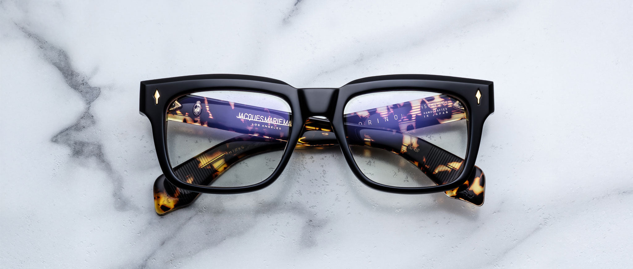 Jacques Marie Mage Torino in Borneo Tavern tortoise optical frame, front view with lights reflected in lenses on a white marble surface.