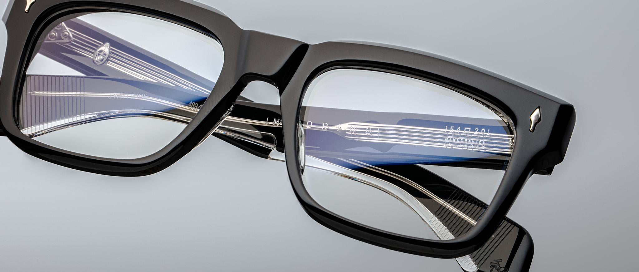 Close-up of Jacques Marie Mage Torino bold rectangular eyeglass frames, with a blue and silver fountain pen reflected in the lenses against a light gray background—showcasing the refined, handcrafted acetate eyewear by Jacques Marie Mage.