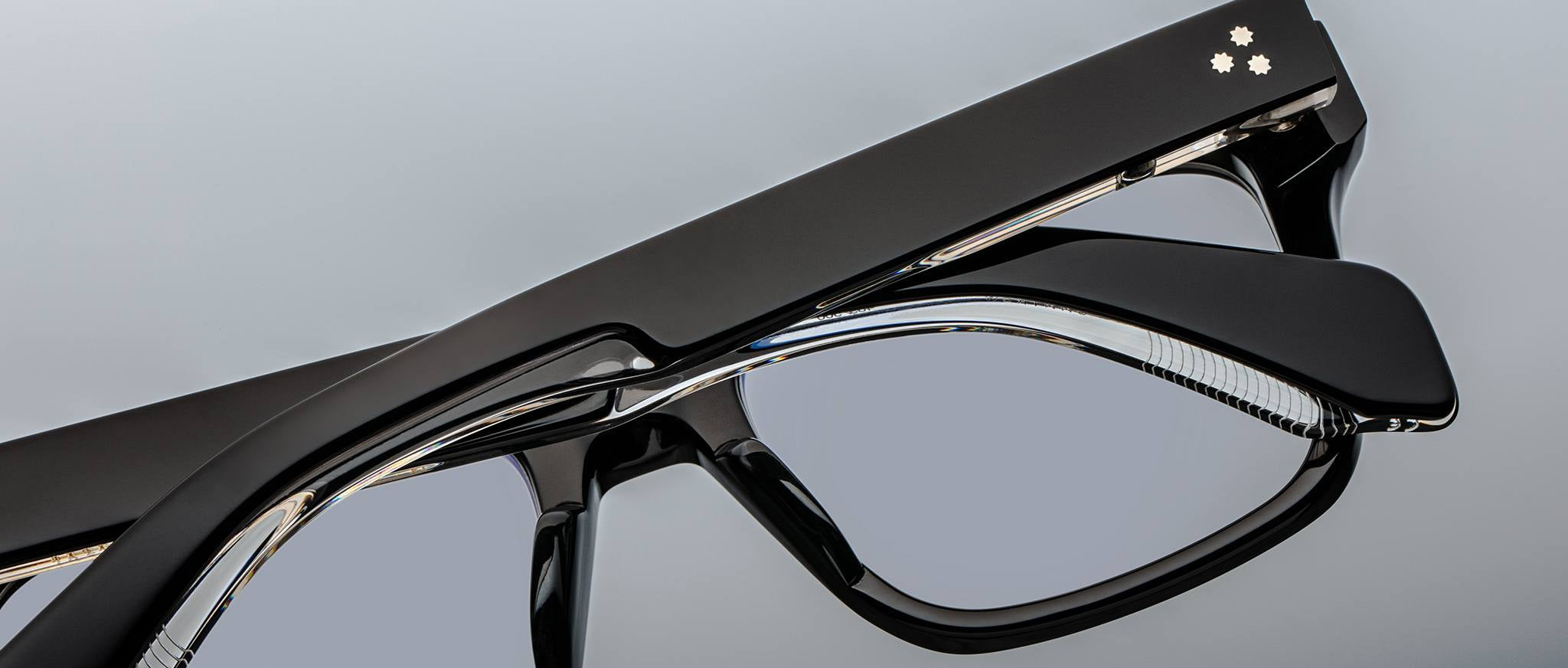 Close-up of two Jacques Marie Mage Torino rectangular eyeglass frames stacked together, showcasing the brand's handcrafted acetate and clear lenses against a gray background.