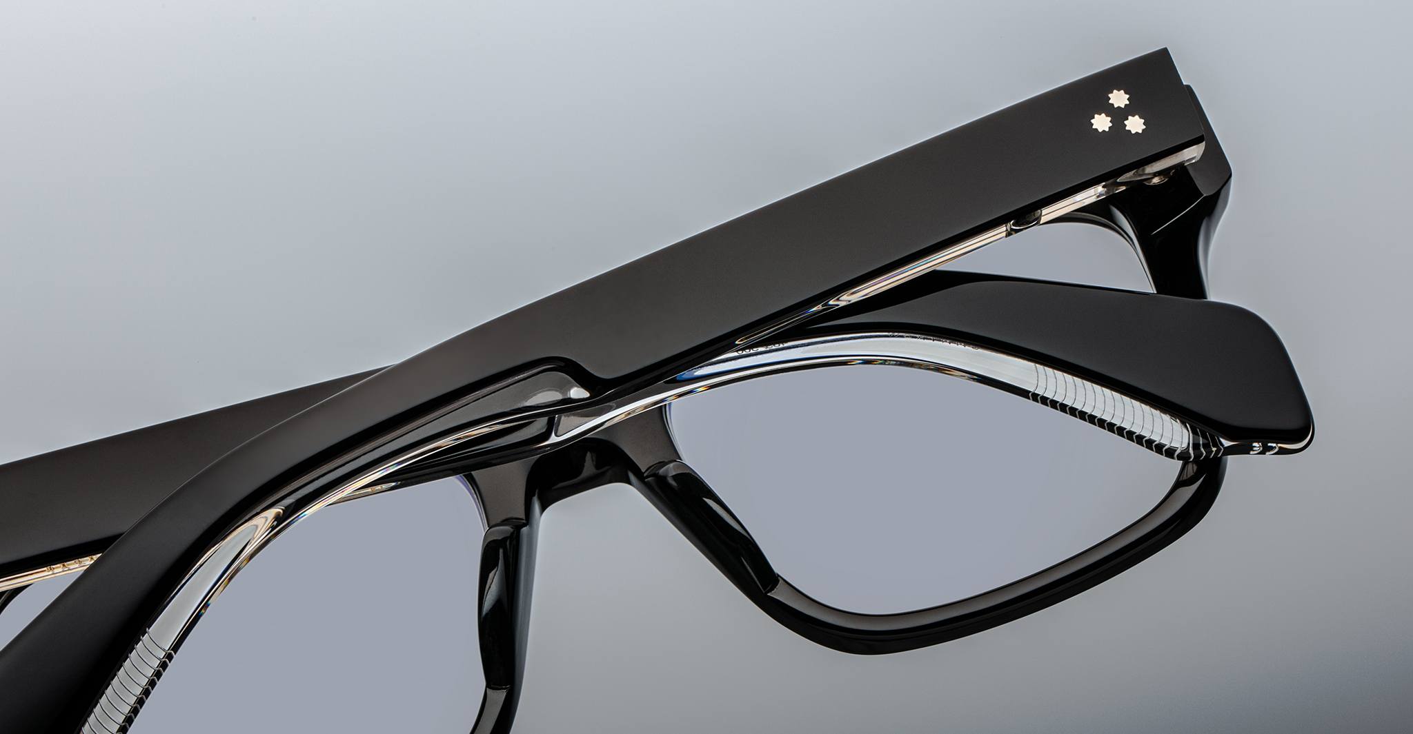 Close-up of two Jacques Marie Mage Torino rectangular eyeglass frames stacked together, showcasing the brand's handcrafted acetate and clear lenses against a gray background.