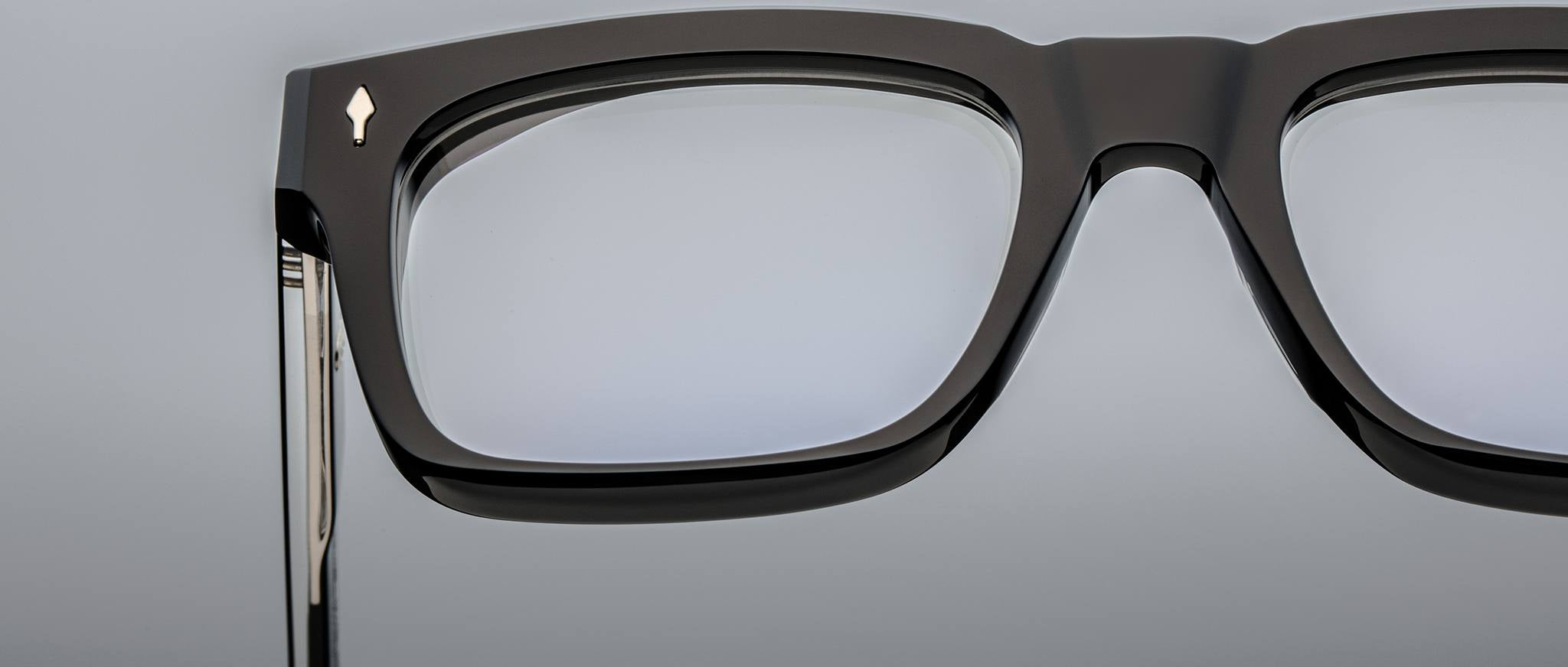 Close-up of the upper left section of bold rectangular Jacques Marie Mage Torino eyewear, handcrafted from acetate, featuring a metallic arrow detail near the hinge.