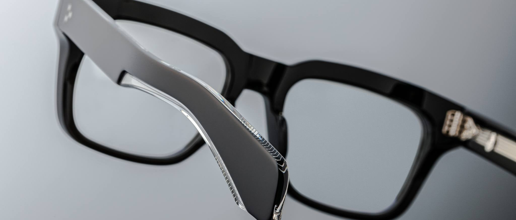 Close-up view of Jacques Marie Mage Torino bold rectangular eyeglass frames, highlighting the metallic hinge detail of handcrafted acetate eyewear by Jacques Marie Mage on a neutral background.