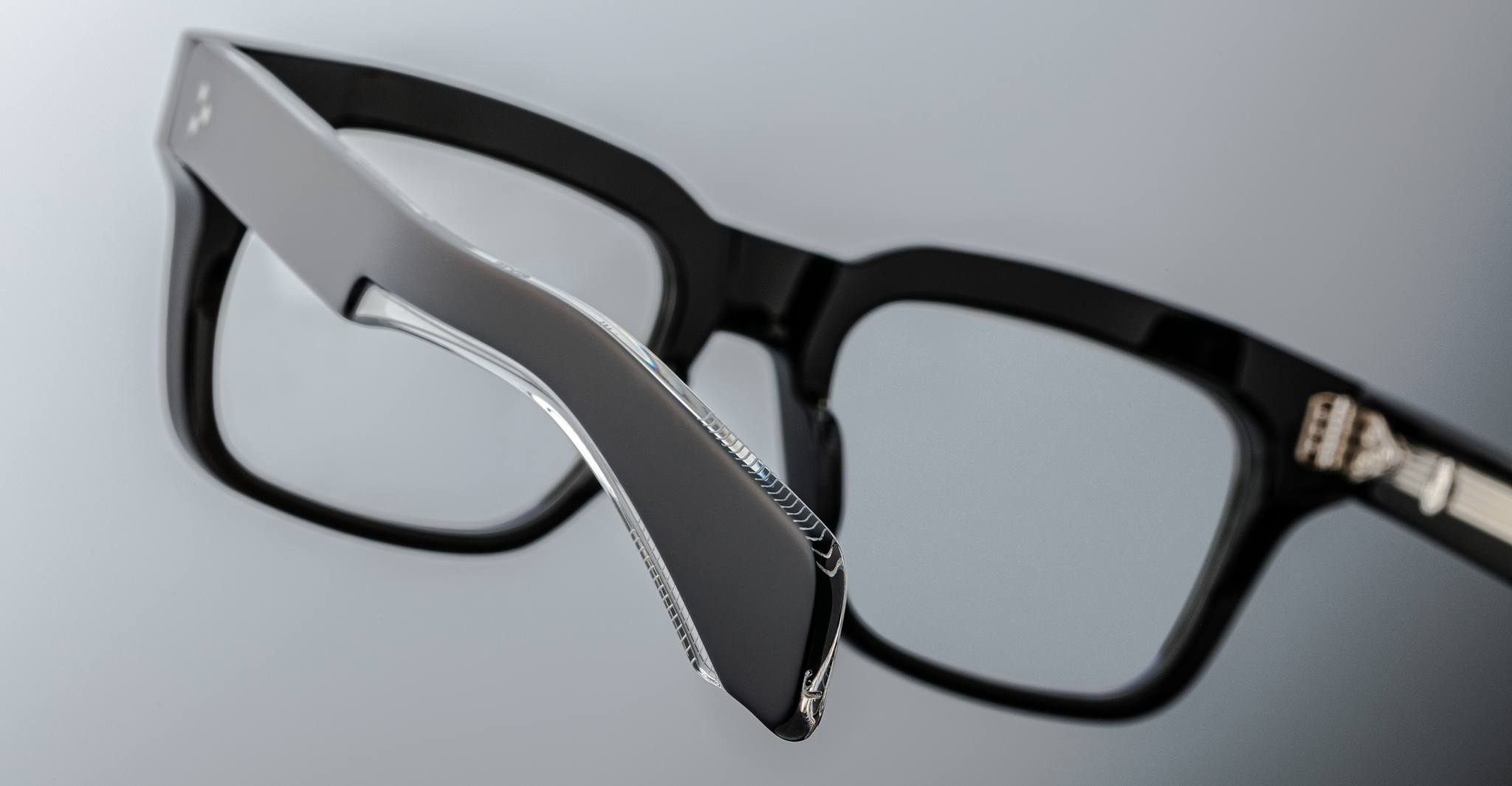 Close-up view of Jacques Marie Mage Torino bold rectangular eyeglass frames, highlighting the metallic hinge detail of handcrafted acetate eyewear by Jacques Marie Mage on a neutral background.