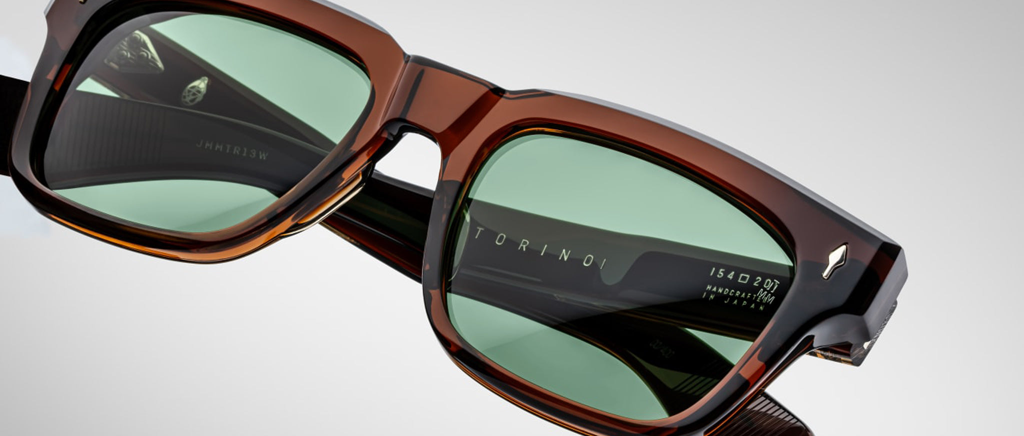 Close-up of Jacques Marie Mage Torino bold rectangular eyeglass frames in brown acetate with green lenses, featuring "TORINO" on the inner frame and size details on the temple by Jacques Marie Mage.