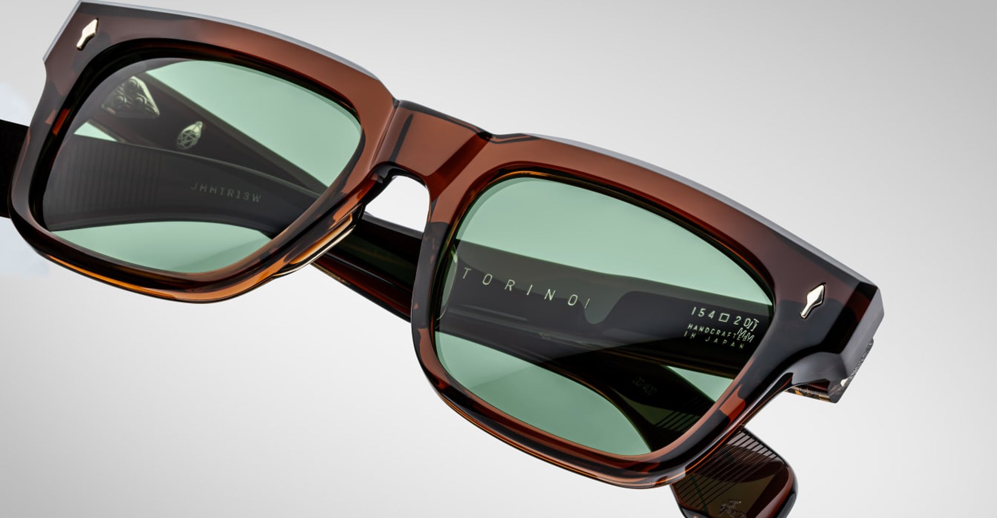 Close-up of Jacques Marie Mage Torino bold rectangular eyeglass frames in brown acetate with green lenses, featuring "TORINO" on the inner frame and size details on the temple by Jacques Marie Mage.