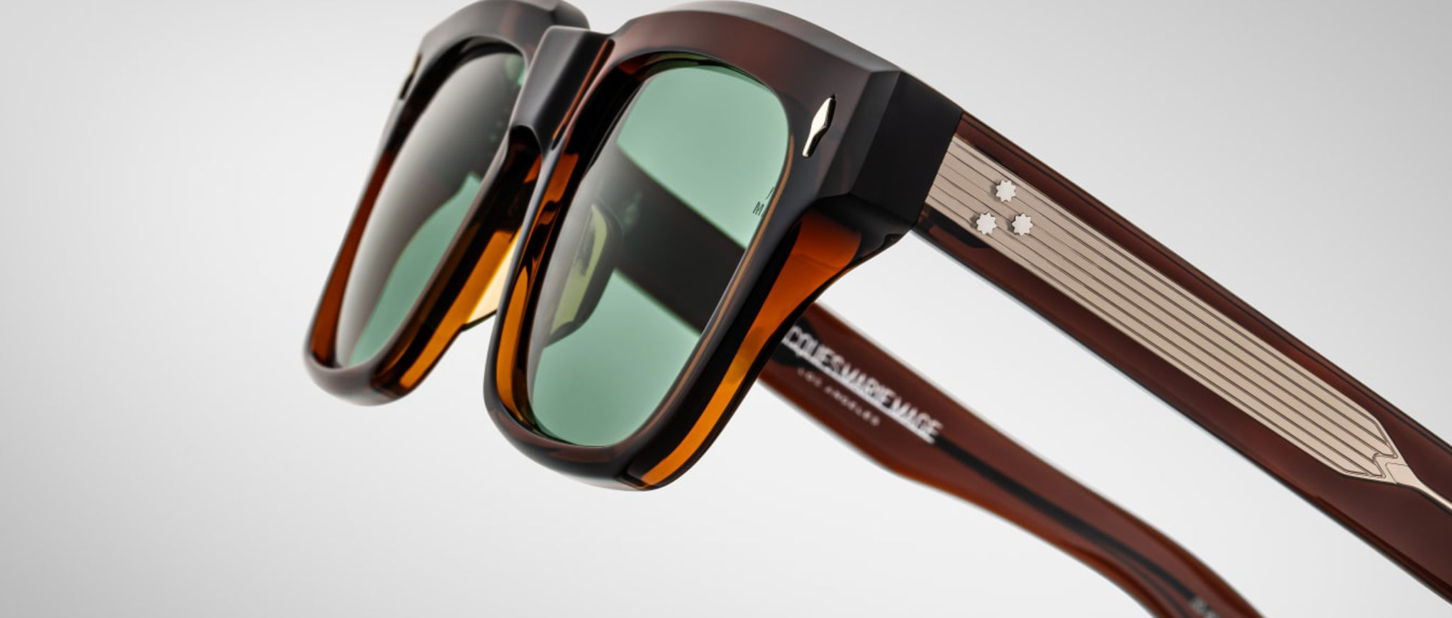 Close-up of Jacques Marie Mage Torino rectangular acetate eyeglass frames with green lenses and metallic star accents, inspired by the brand’s iconic style, set against a plain light background.