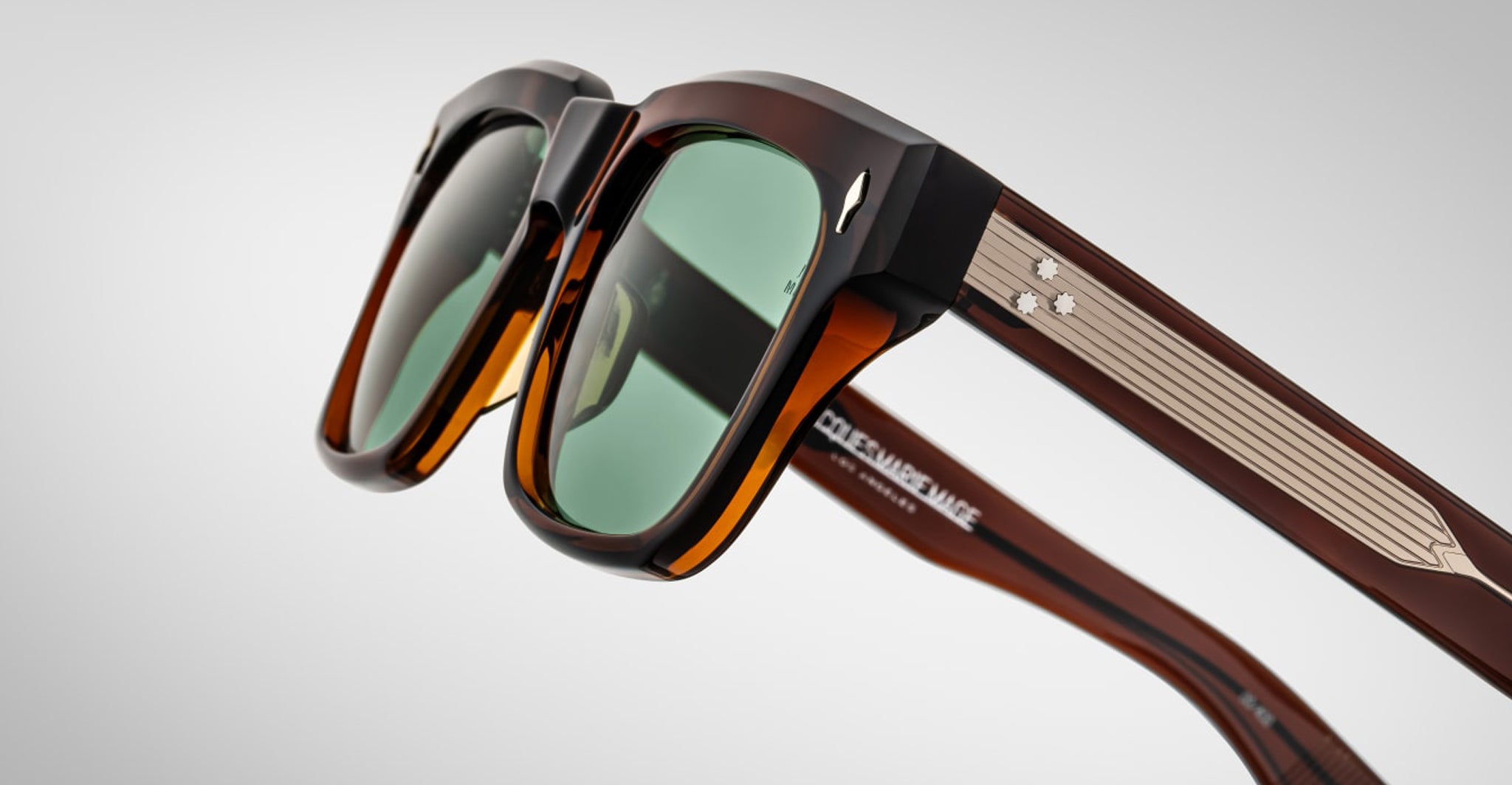 Close-up of Jacques Marie Mage Torino rectangular acetate eyeglass frames with green lenses and metallic star accents, inspired by the brand’s iconic style, set against a plain light background.